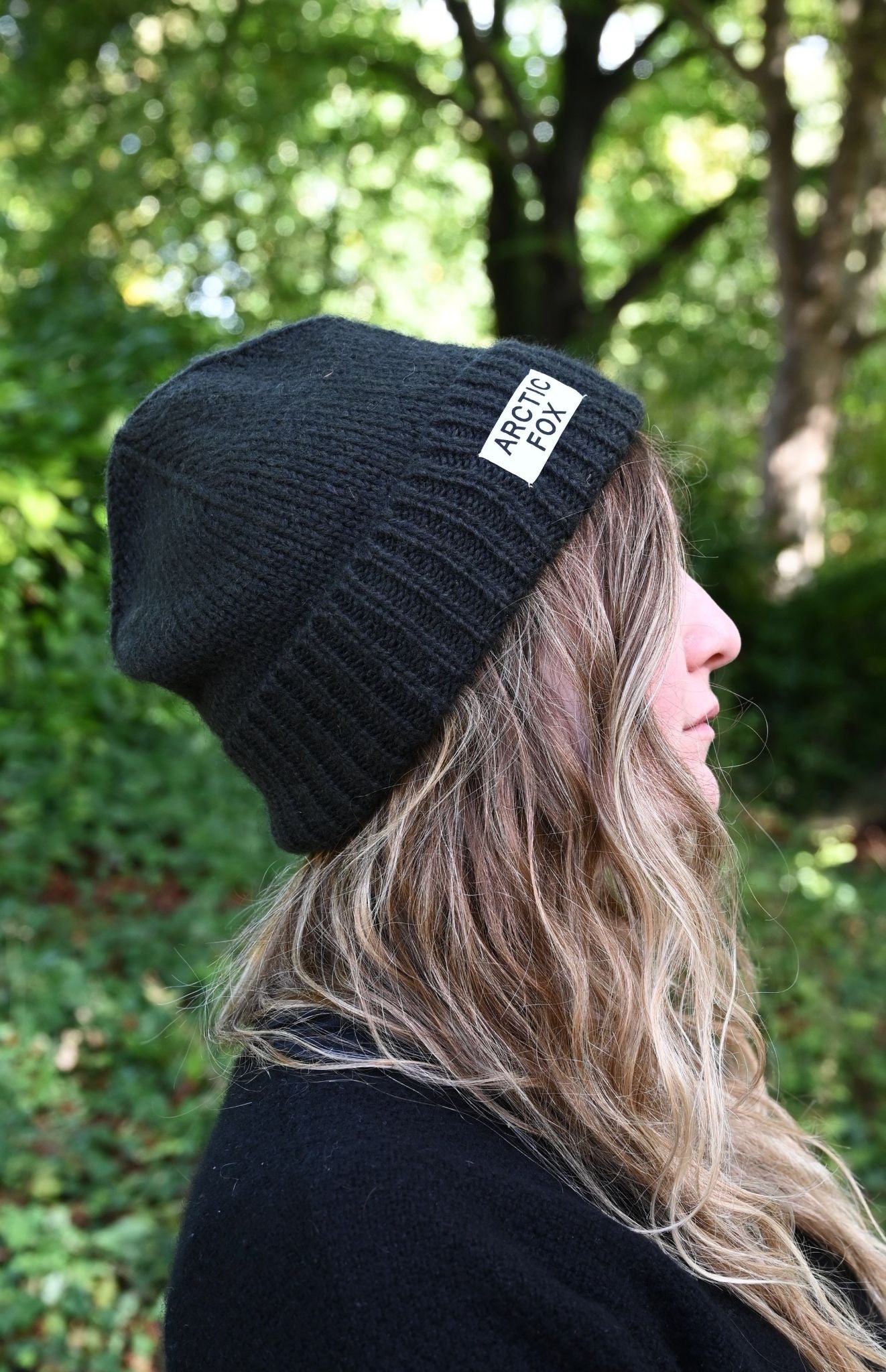 Person wearing a black beanie with a brand logo outdoors