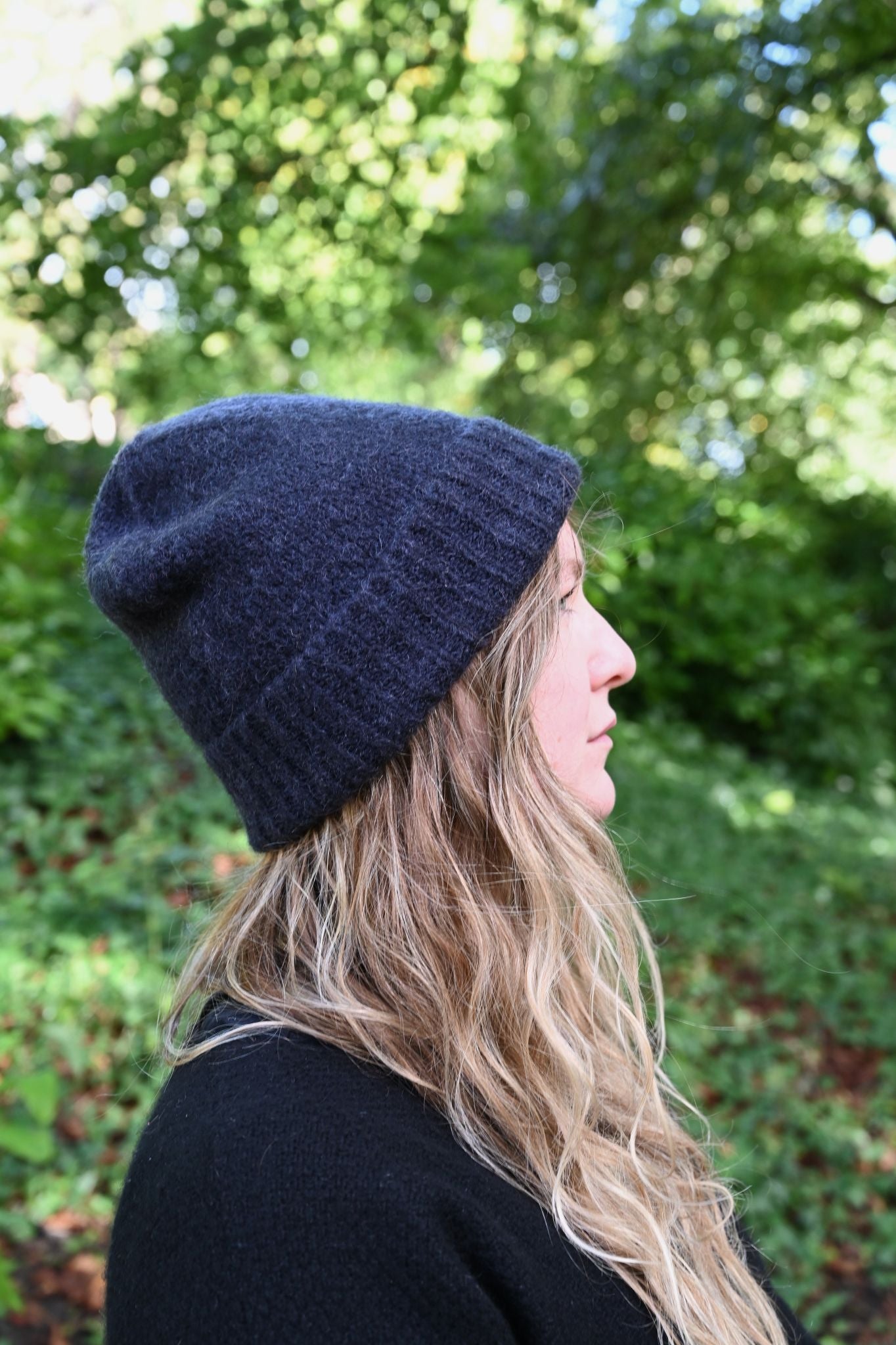 Person wearing a navy blue beanie in a natural setting with greenery.