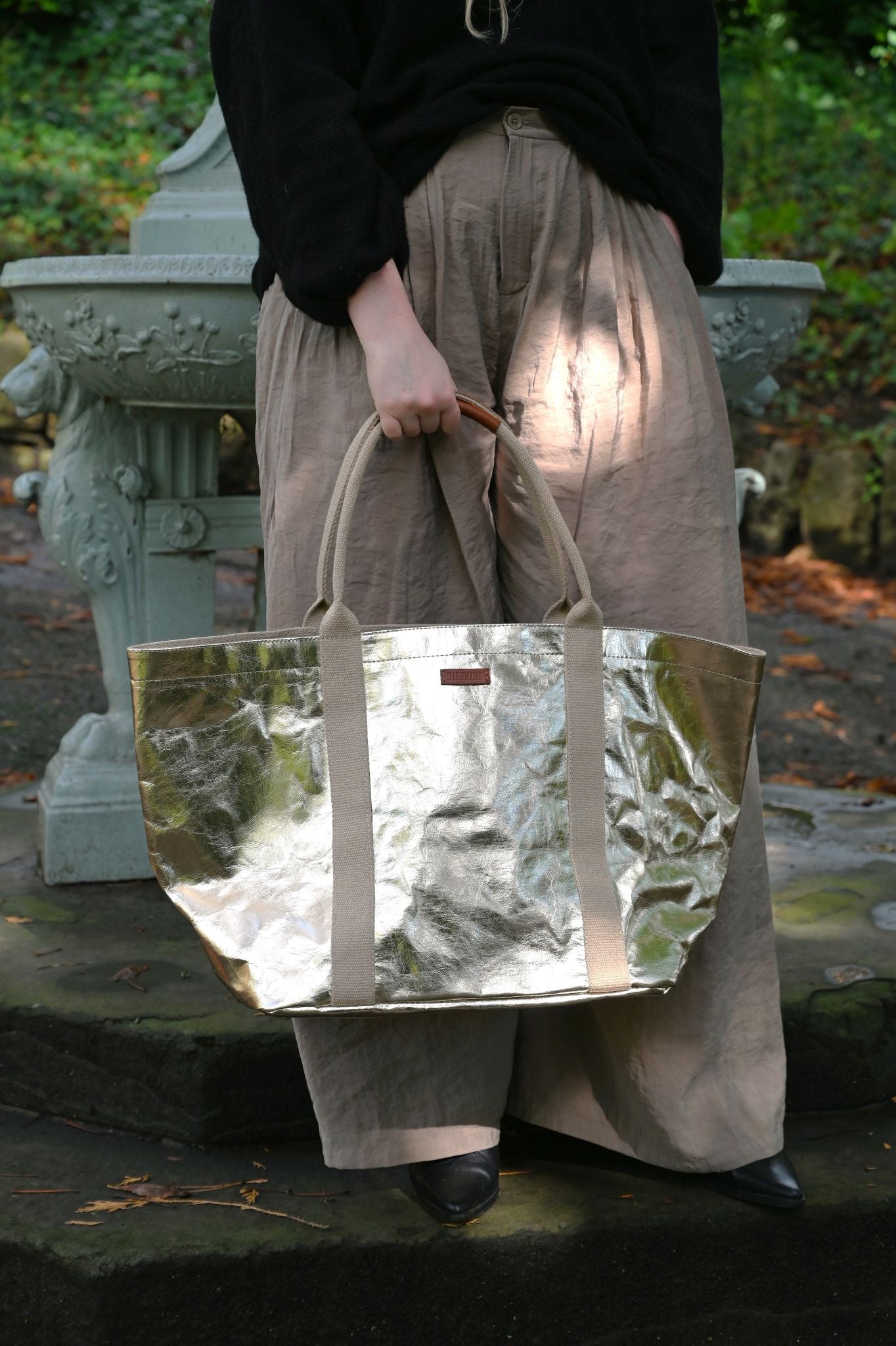 Person holding a reflective pale gold tote bag outdoors