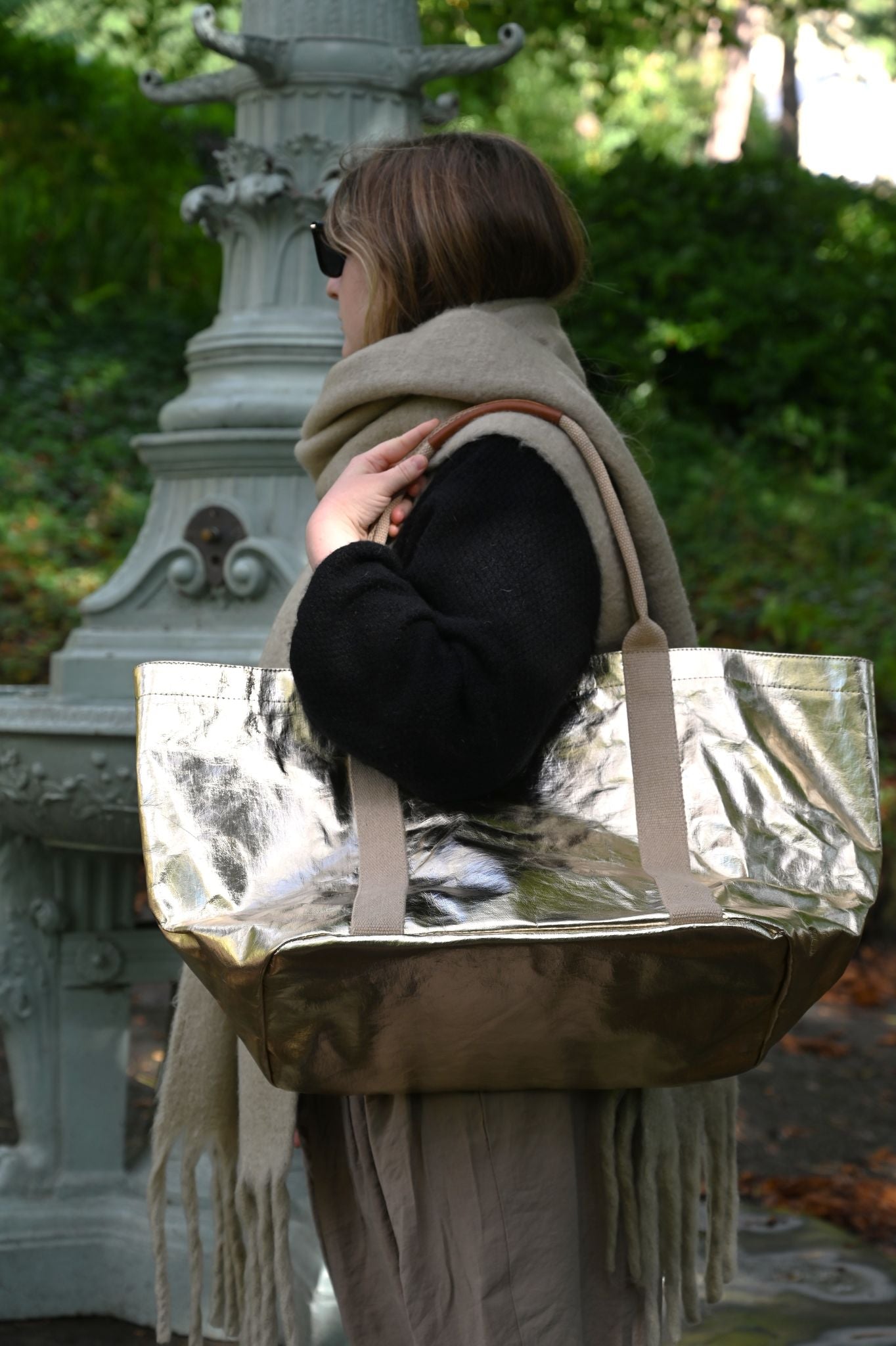 Person holding a siny pale gold tote bag in an outdoor setting