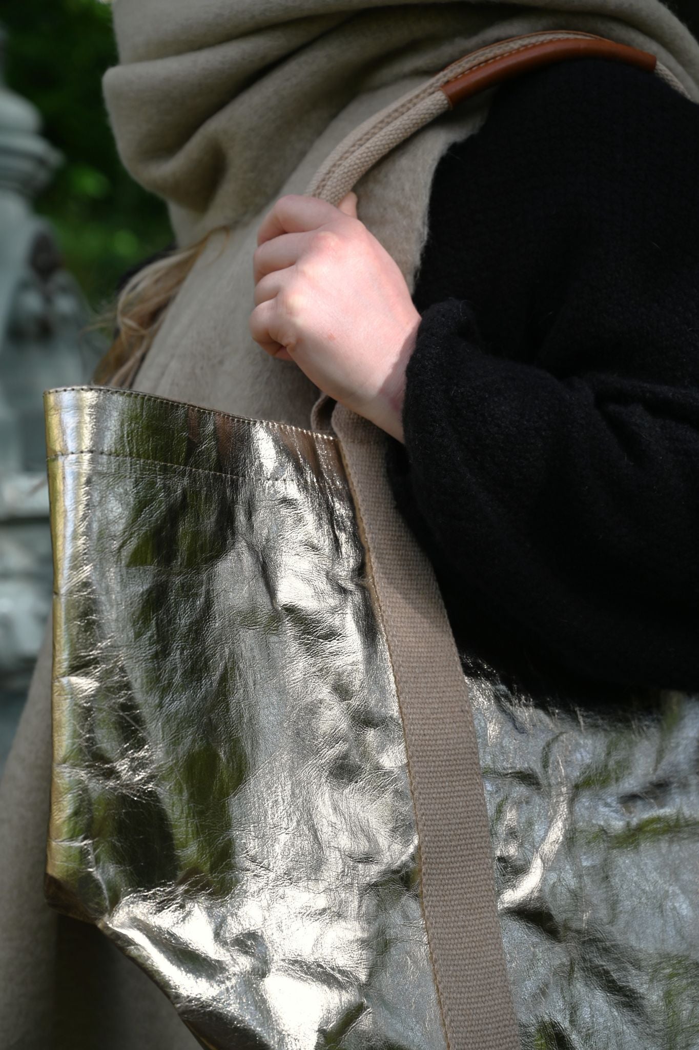 Person holding a metallic pale gold bag with a blurred background