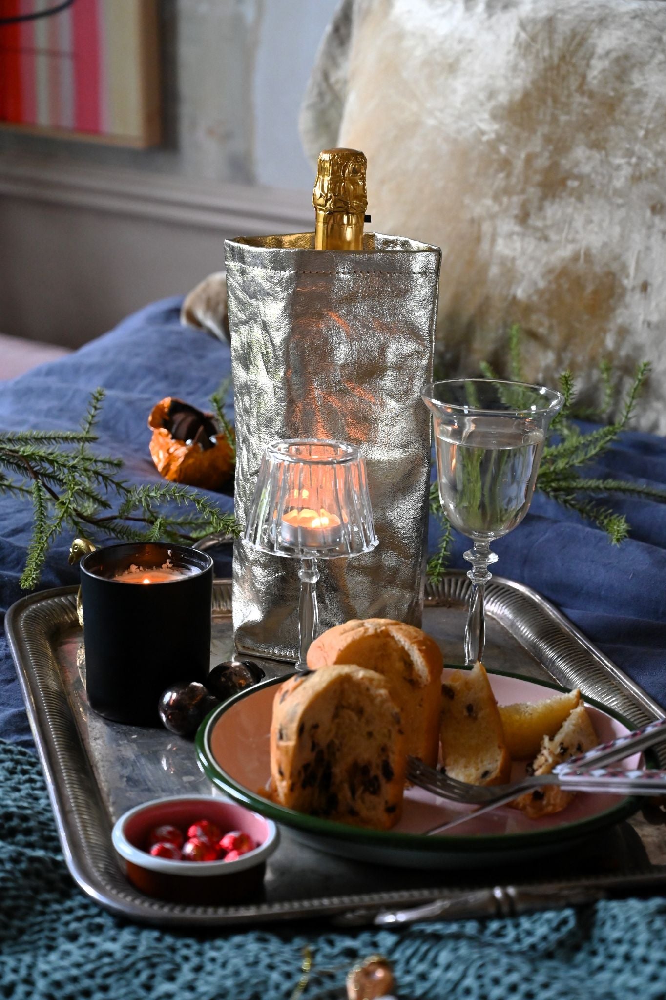 Tray with pastries, wine glasses, and a bottle of champagne in a metallic paper wine cooler on a decorative surface.