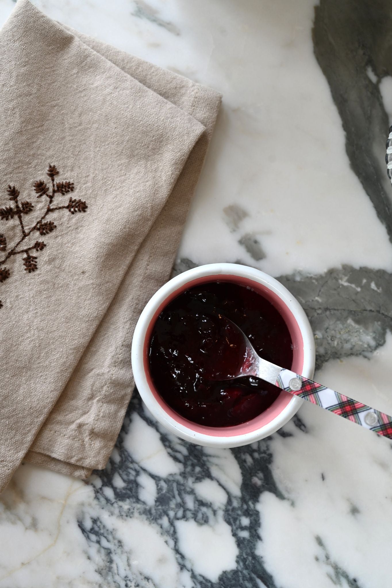 Always Sunday enamel sauce pot of cranberry sauce with a spoon on a marble surface with a pinecone napkin