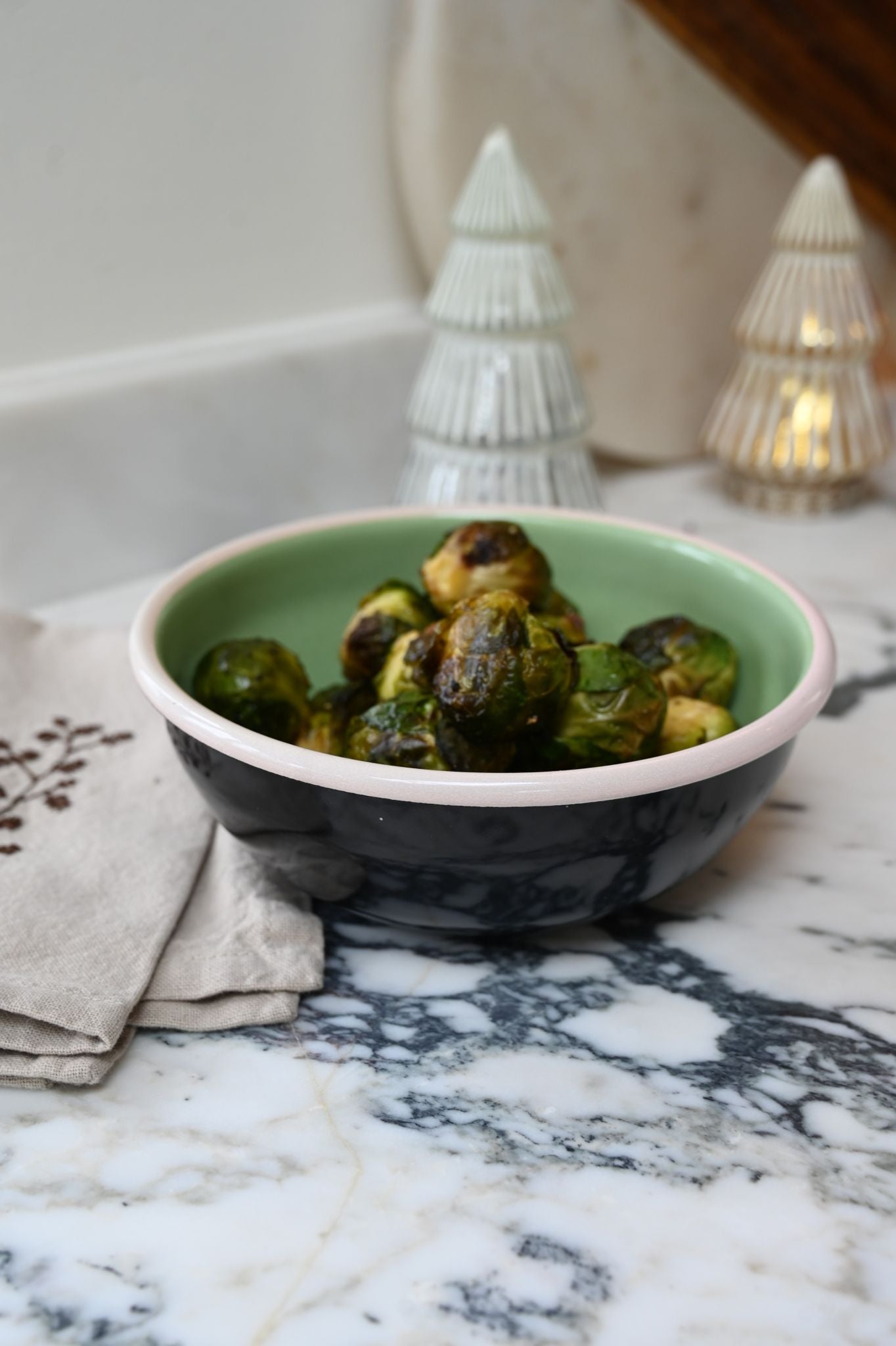 Tricolour enamel serving bowl filled with roasted vegetables on a marble counter.