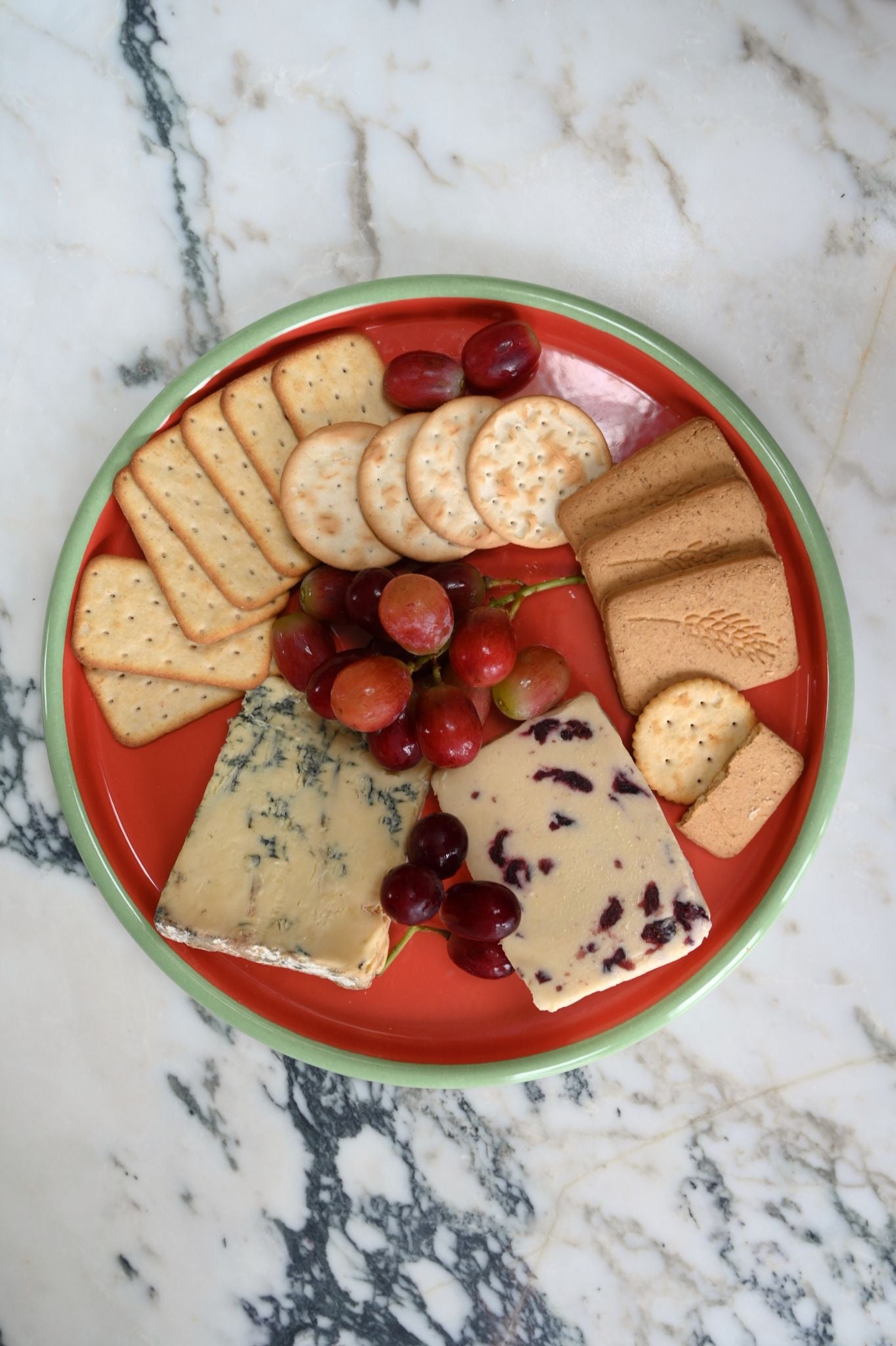 Enamel pizza plate full of assorted cheeses, crackers, and grapes.