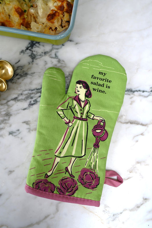 Green oven mitt with a design of a woman holding a watering can and text 'my favorite salad is wine' on a marble surface.