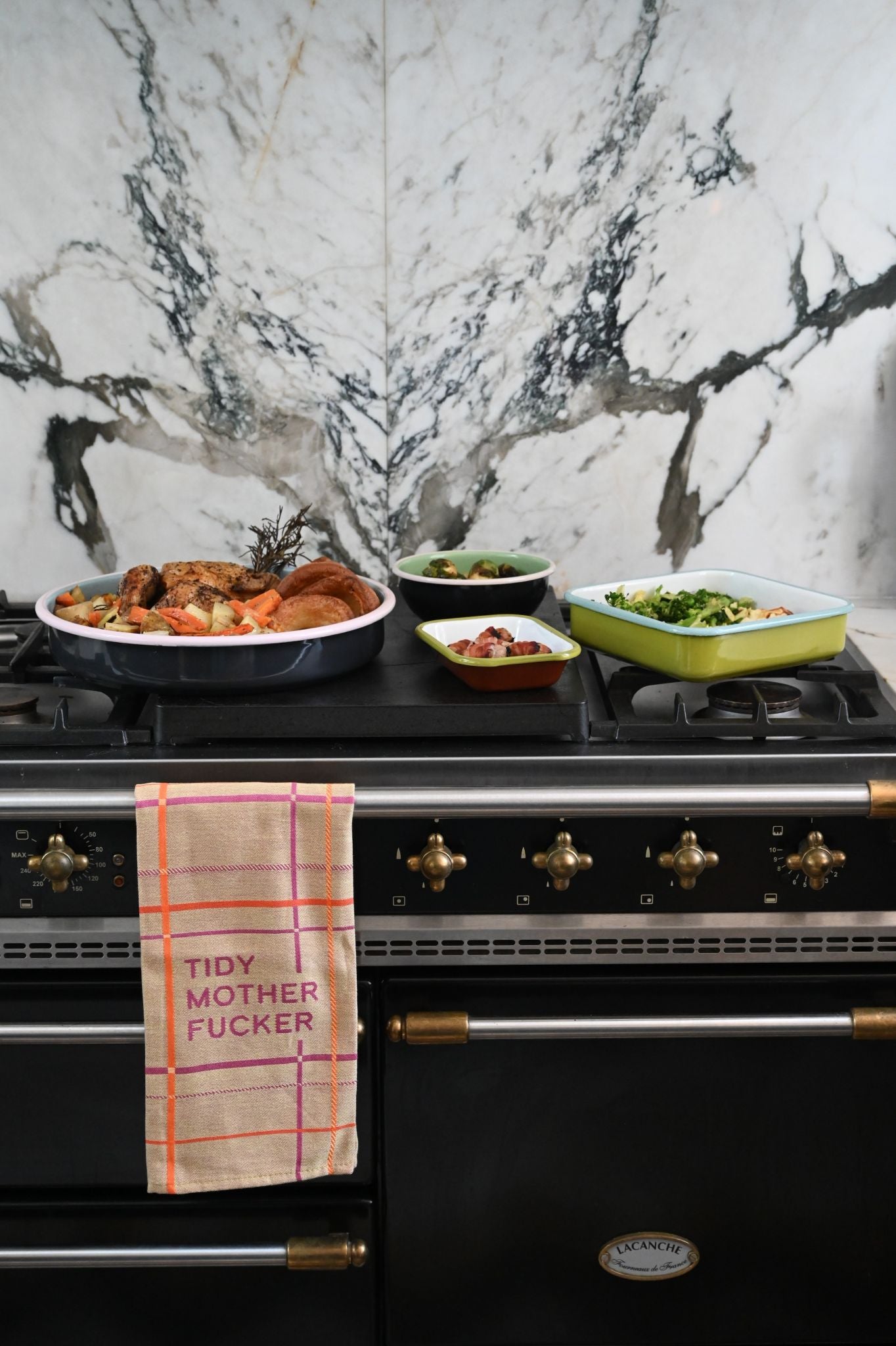Black stove with Always Sunday enamel trays and a decorative tea towel on a marble wall background