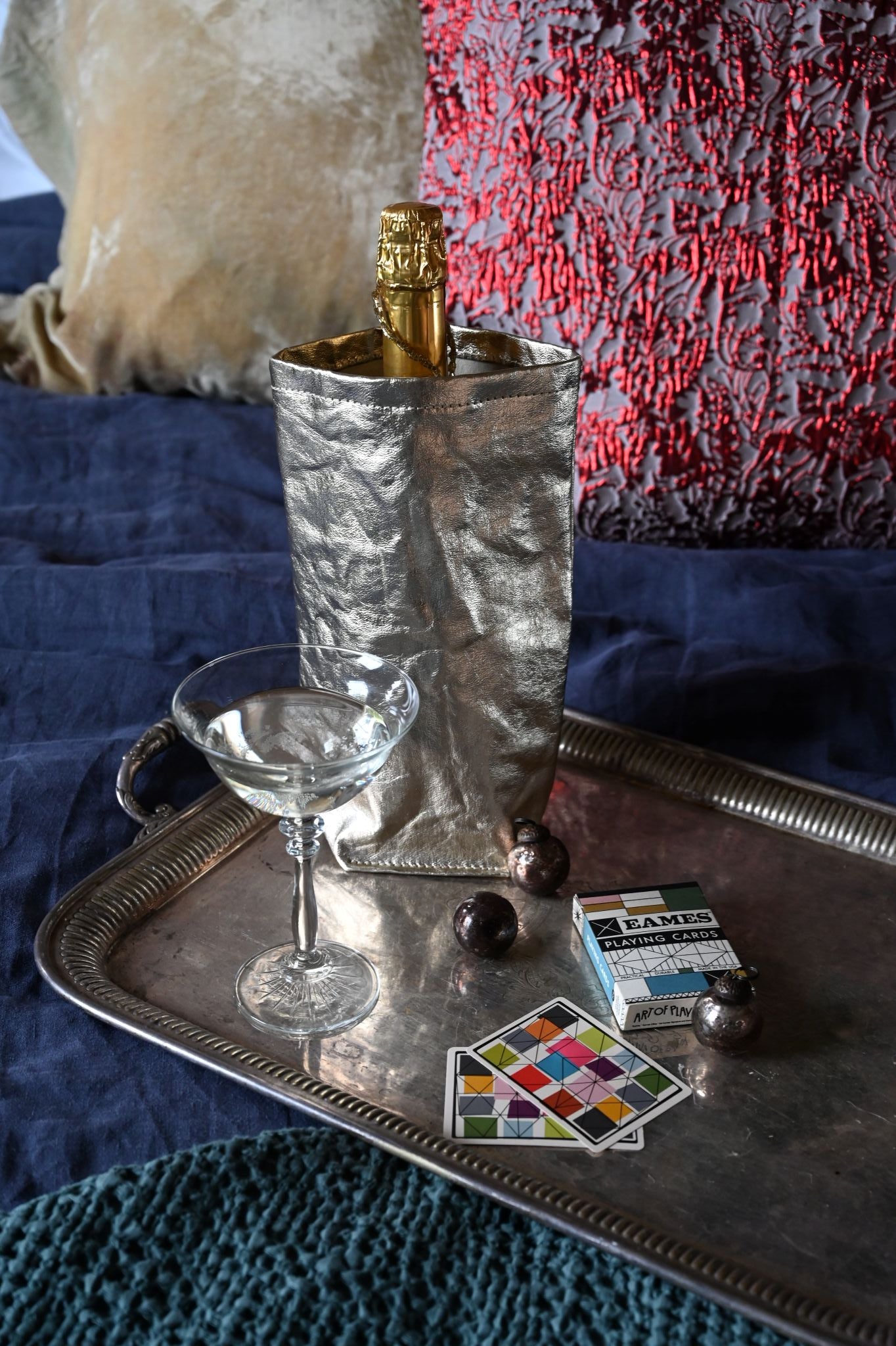 Metallic uashmama wine cooler with coupe glass, eames playing cards and mini glass baubles on a textured surface