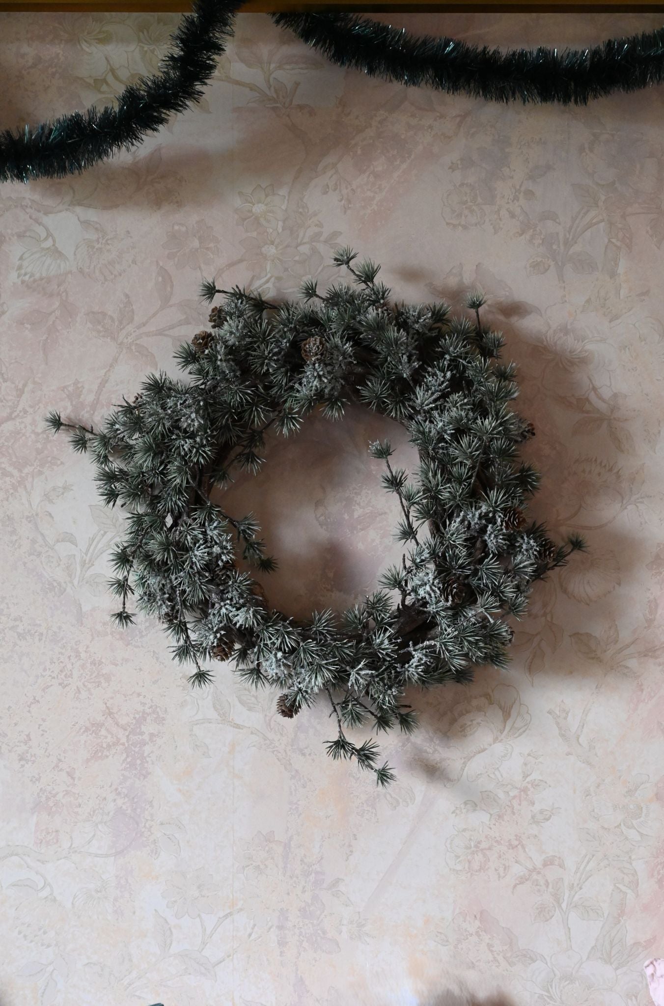 Frosted pinecone wreath on a textured beige surface with tinsel in the background