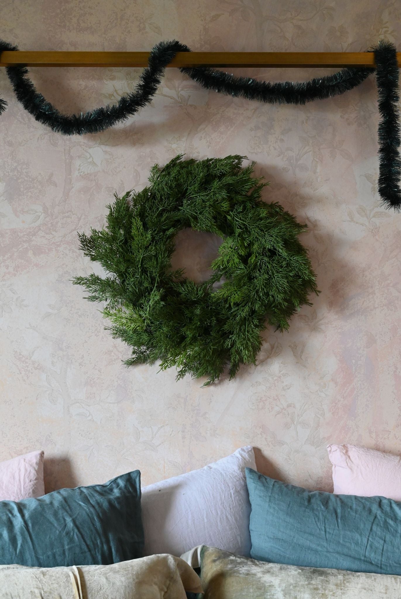 Small green Cyprus wreath on a textured wall with pillows below