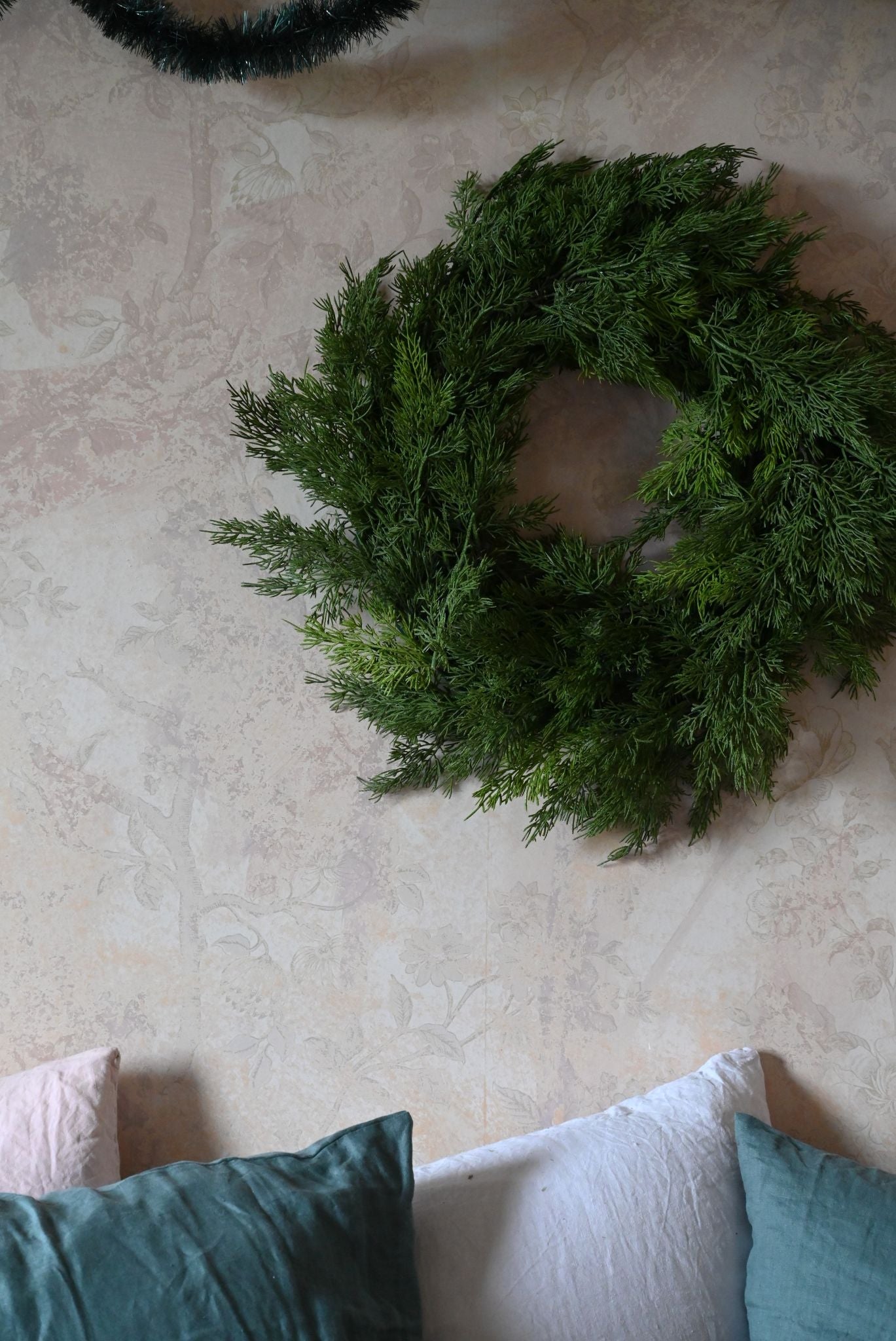 Small green Cyprus wreath on a textured wall with pillows below