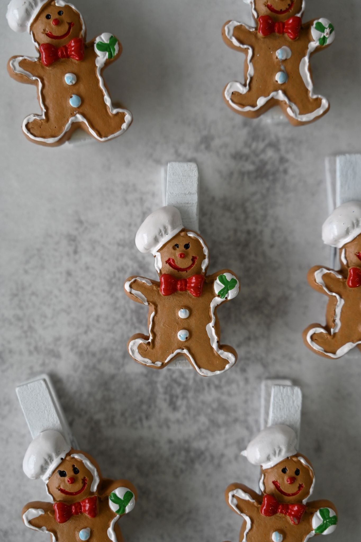 Set of eight wooden clips topped with gingerbread men wearing chef hats and red bow ties.