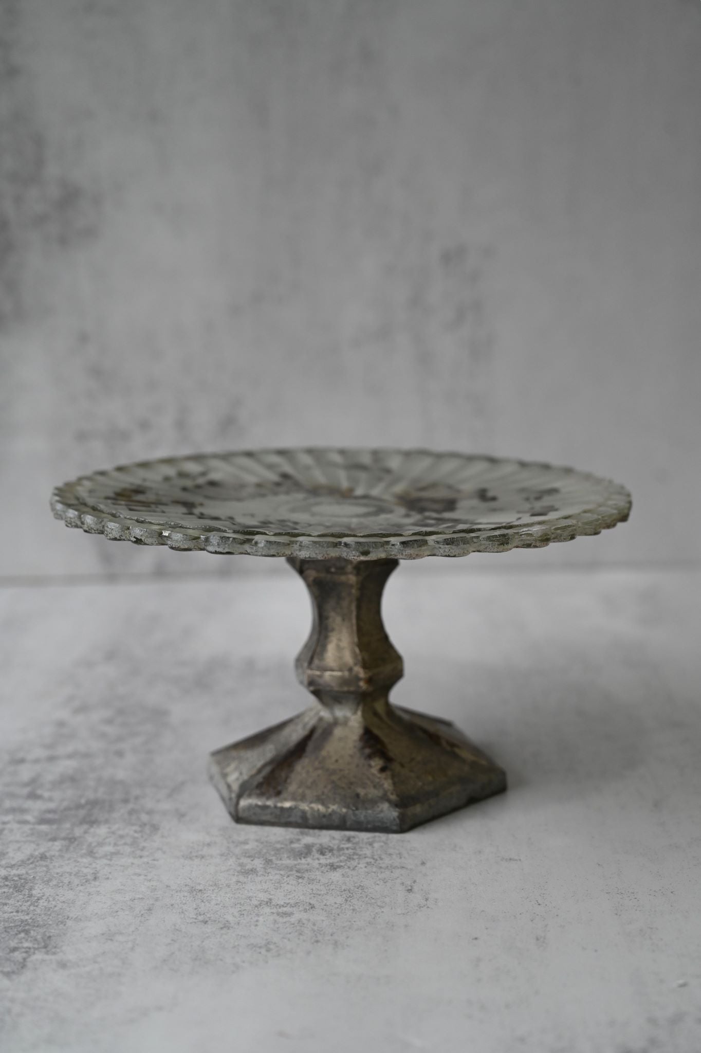 Small antiqued glass pedestal stand with fluted edge and distressed metal base.