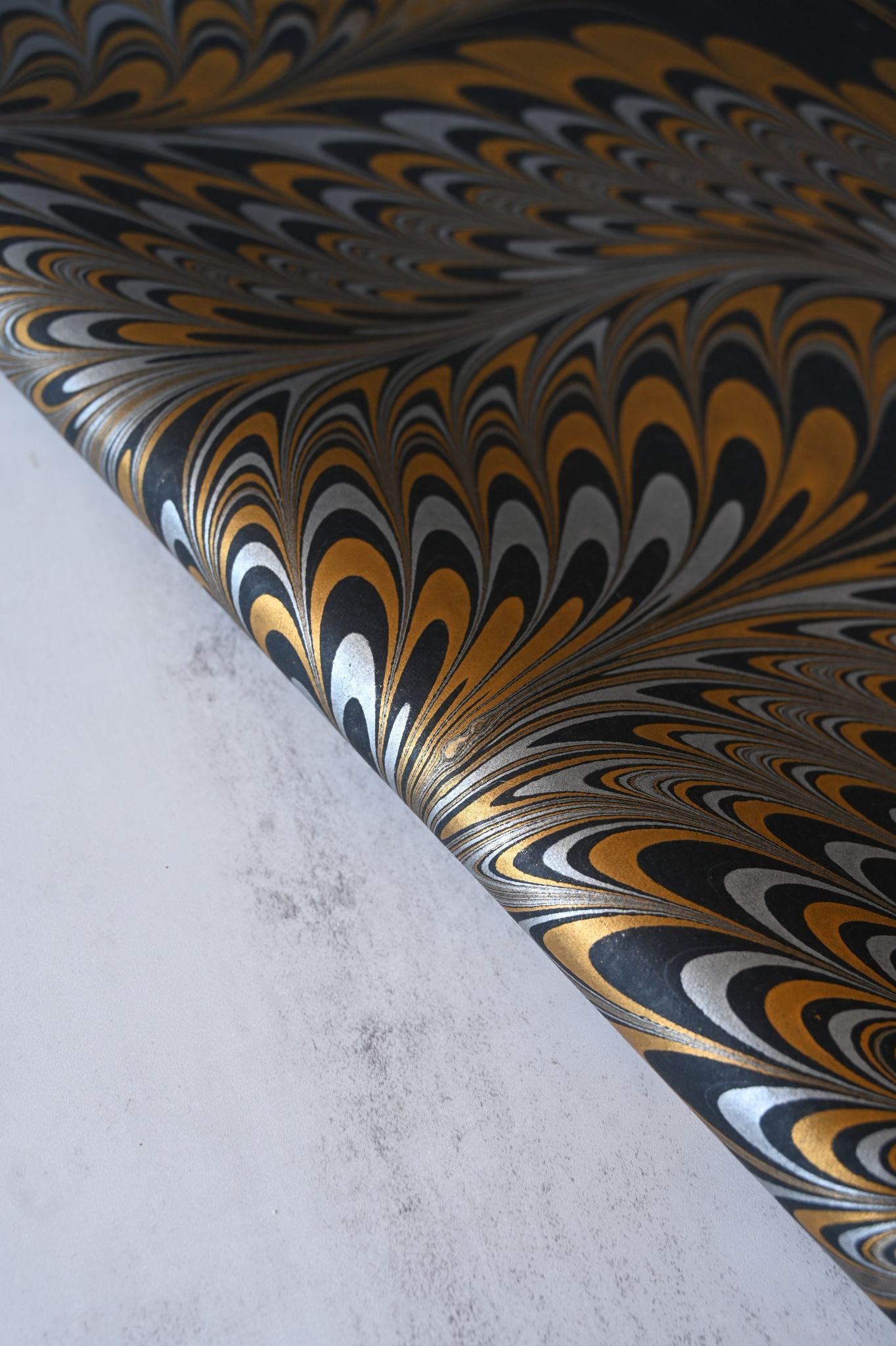 Rolled black and gold metallic marbled paper with a swirling peacock feather design.
