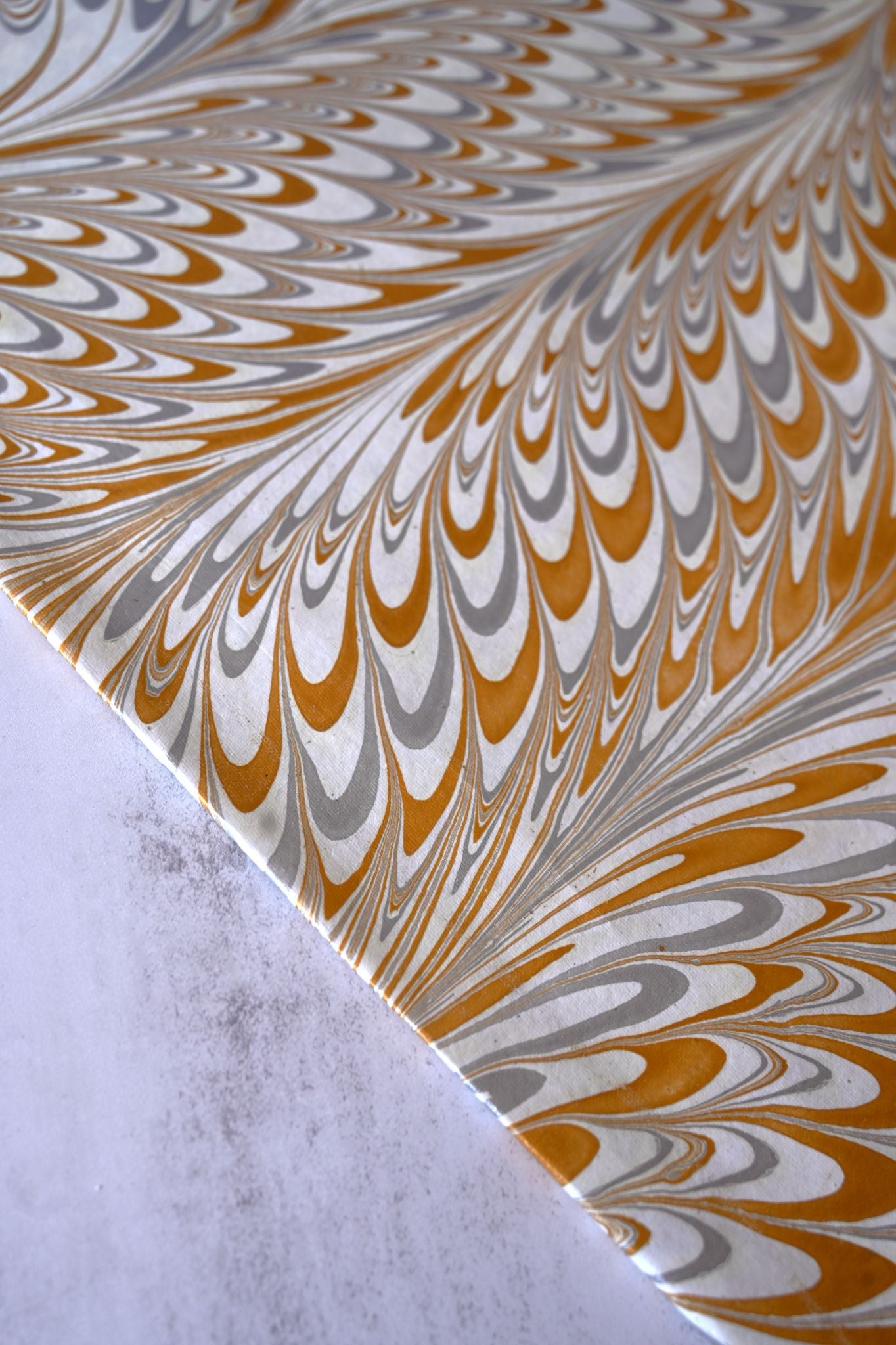 Hand marbled white, gold, and grey paper with intricate peacock feather swirl design.