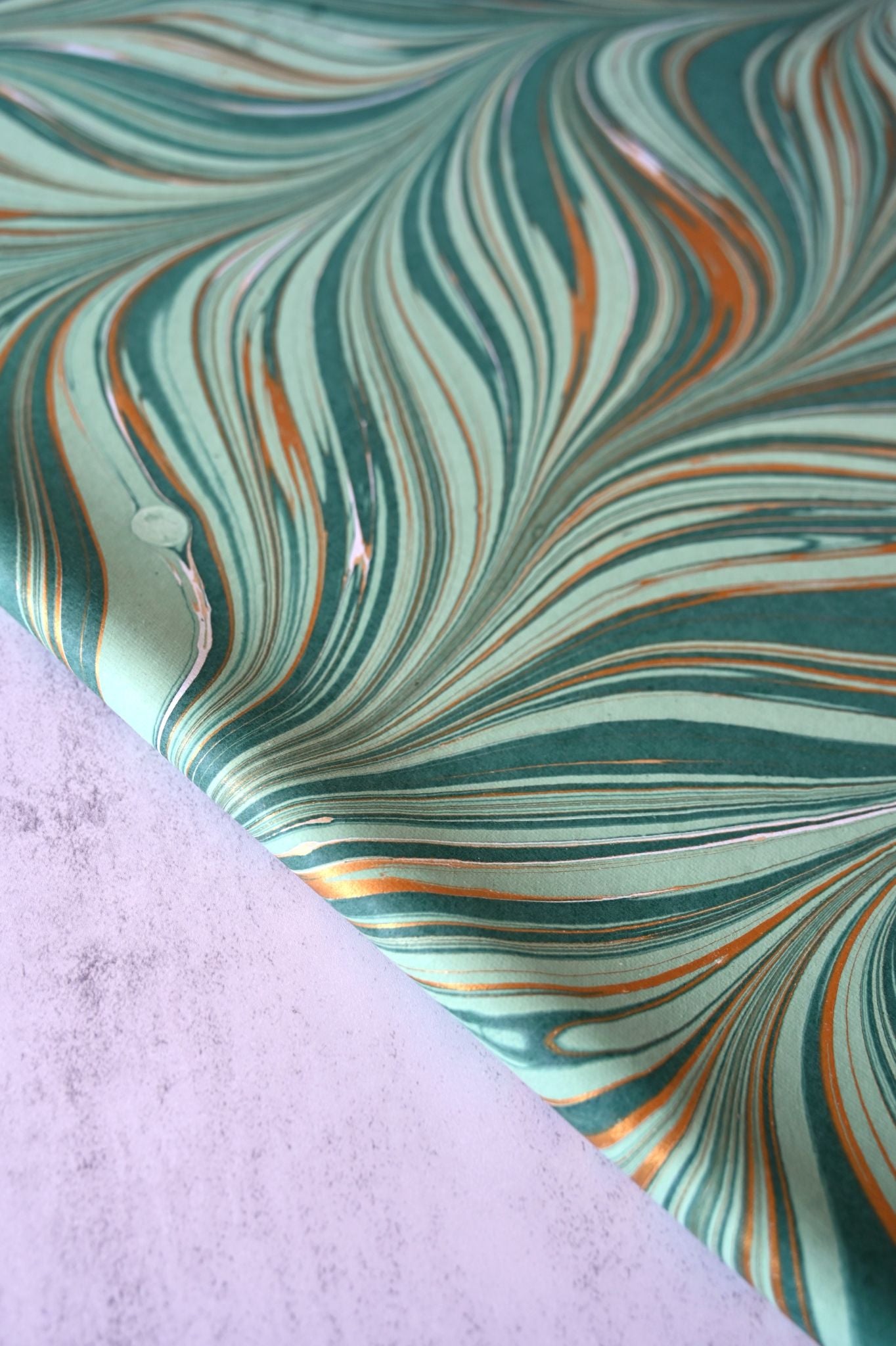 Close-up of luxury mint green and deep green marbled gift wrap with metallic gold swirls.