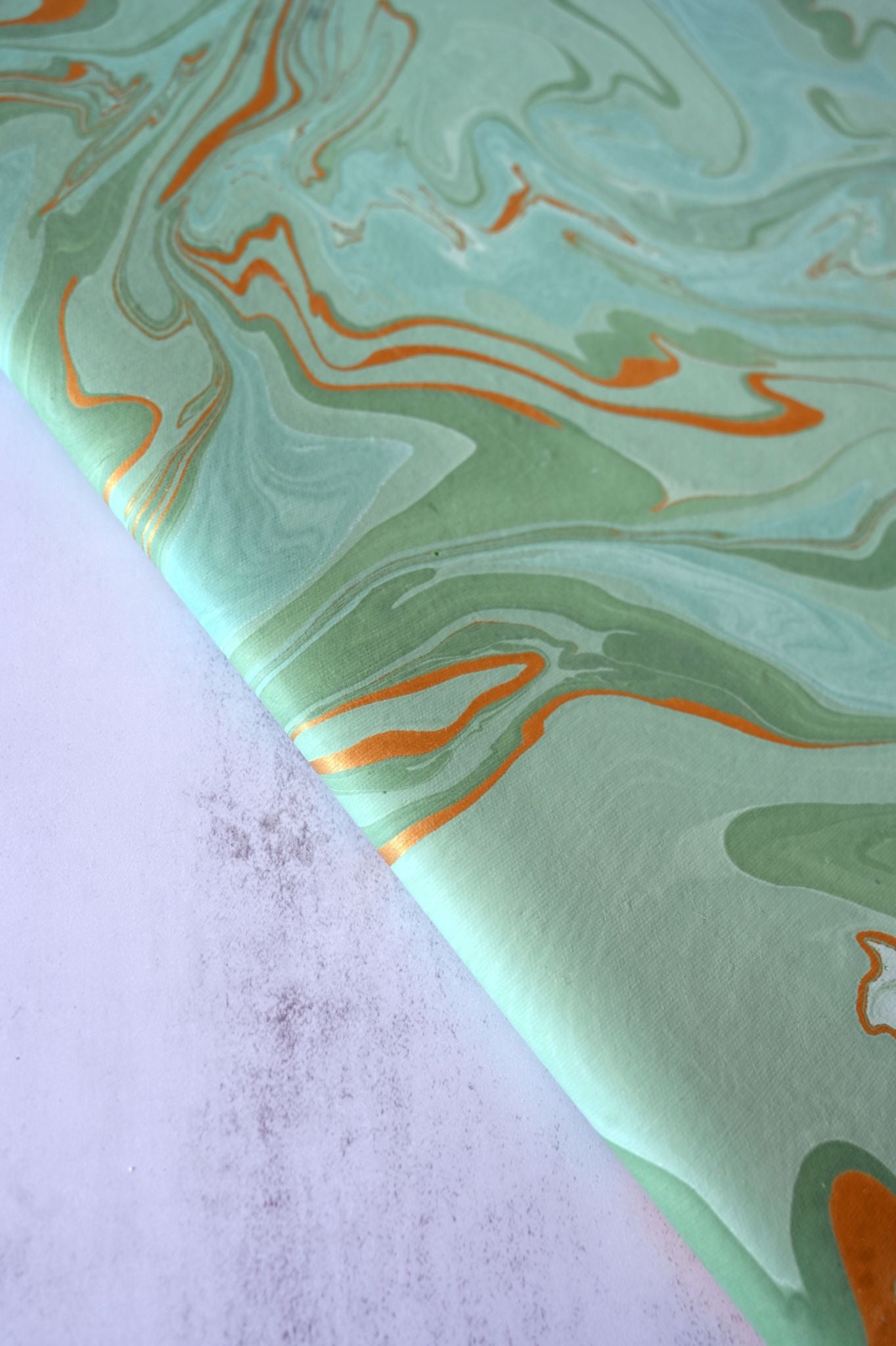 Close-up of green and teal swirl hand-marbled luxury gift wrap with copper lines.