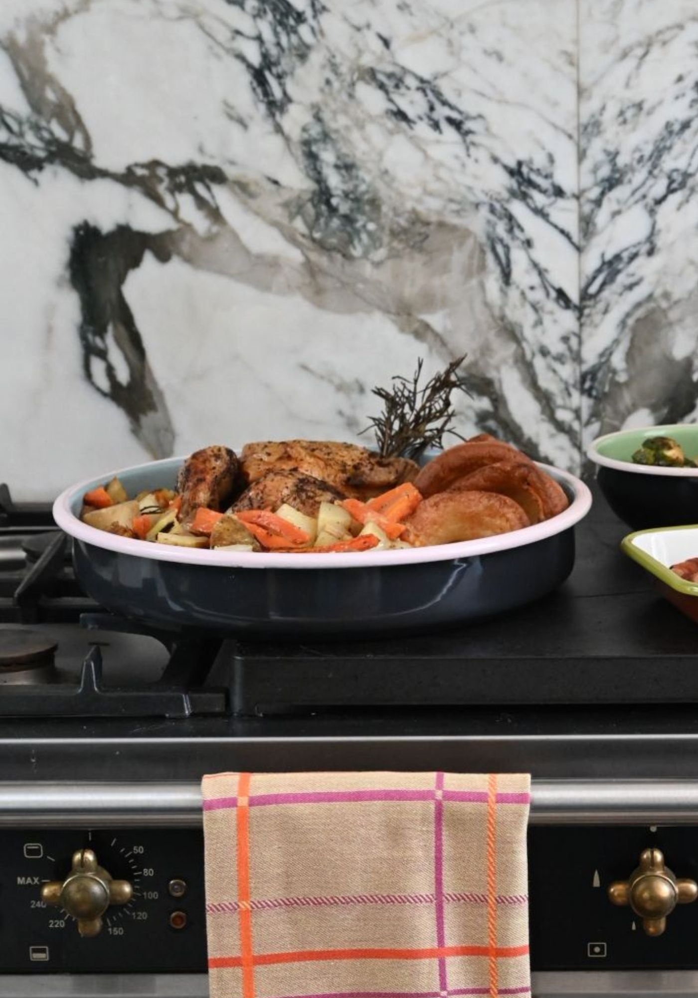 Dark enamel roasting tray filled with roasted chicken and vegetables on a stovetop.