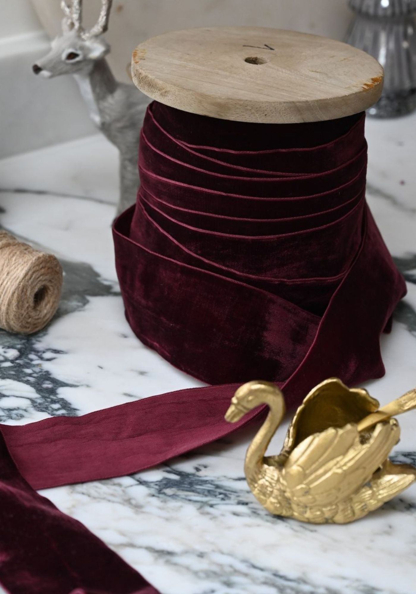 Wide deep purple cotton velvet ribbon wound on a wooden spool on marble.