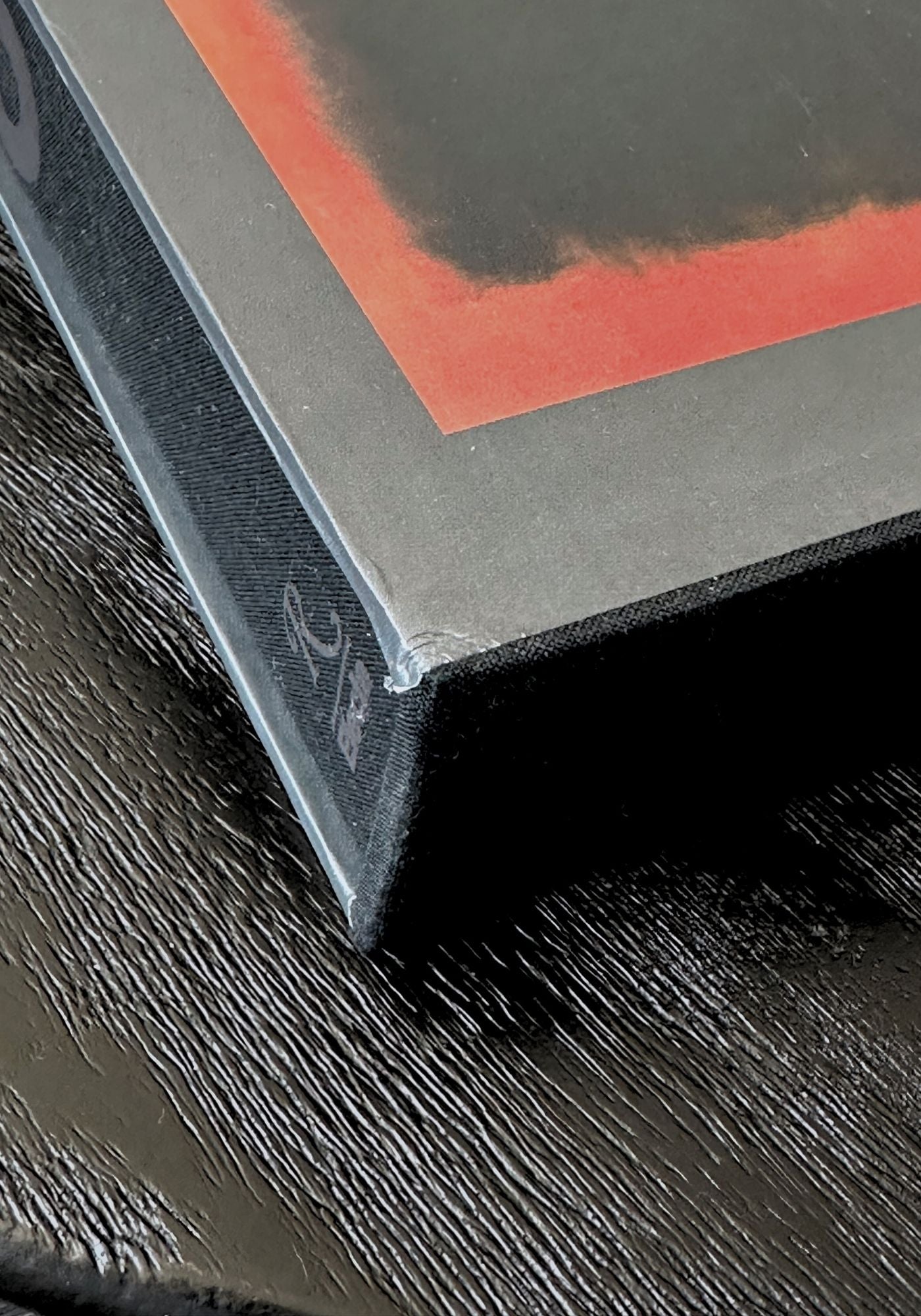 Close-up of a corner of a framed artwork with a red border on a dark surface.