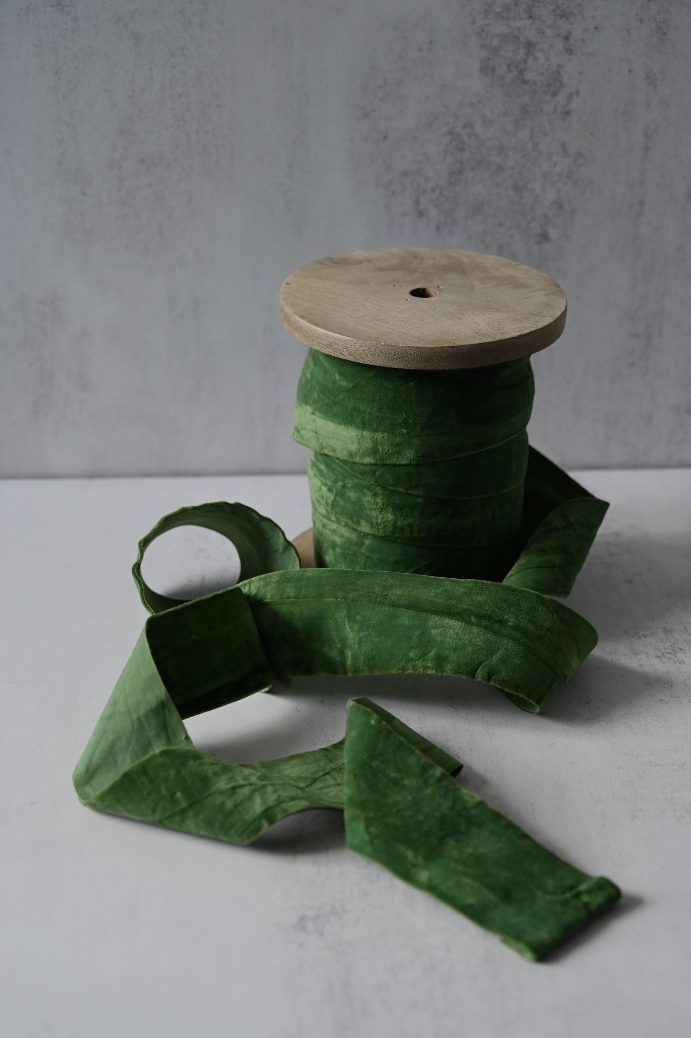 Spool of wide crushed forest green cotton velvet ribbon draped on a surface.