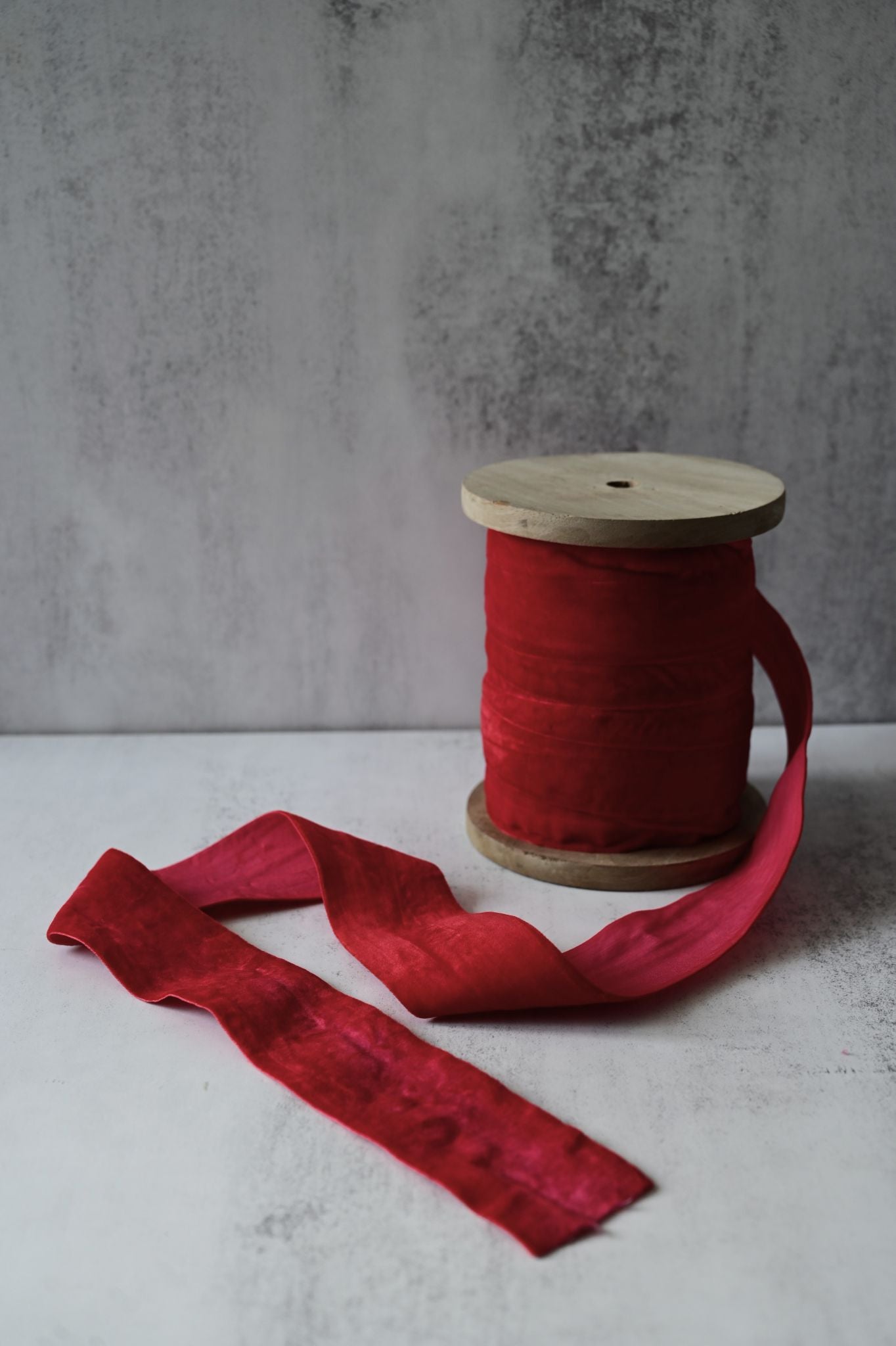 Spool of wide, crushed mulberry red cotton velvet ribbon on a wooden bobbin.
