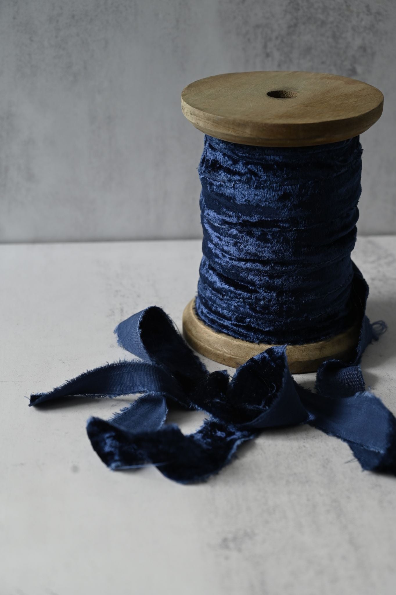 Deep navy blue crushed cotton velvet ribbon with frayed edges on a wooden spool.