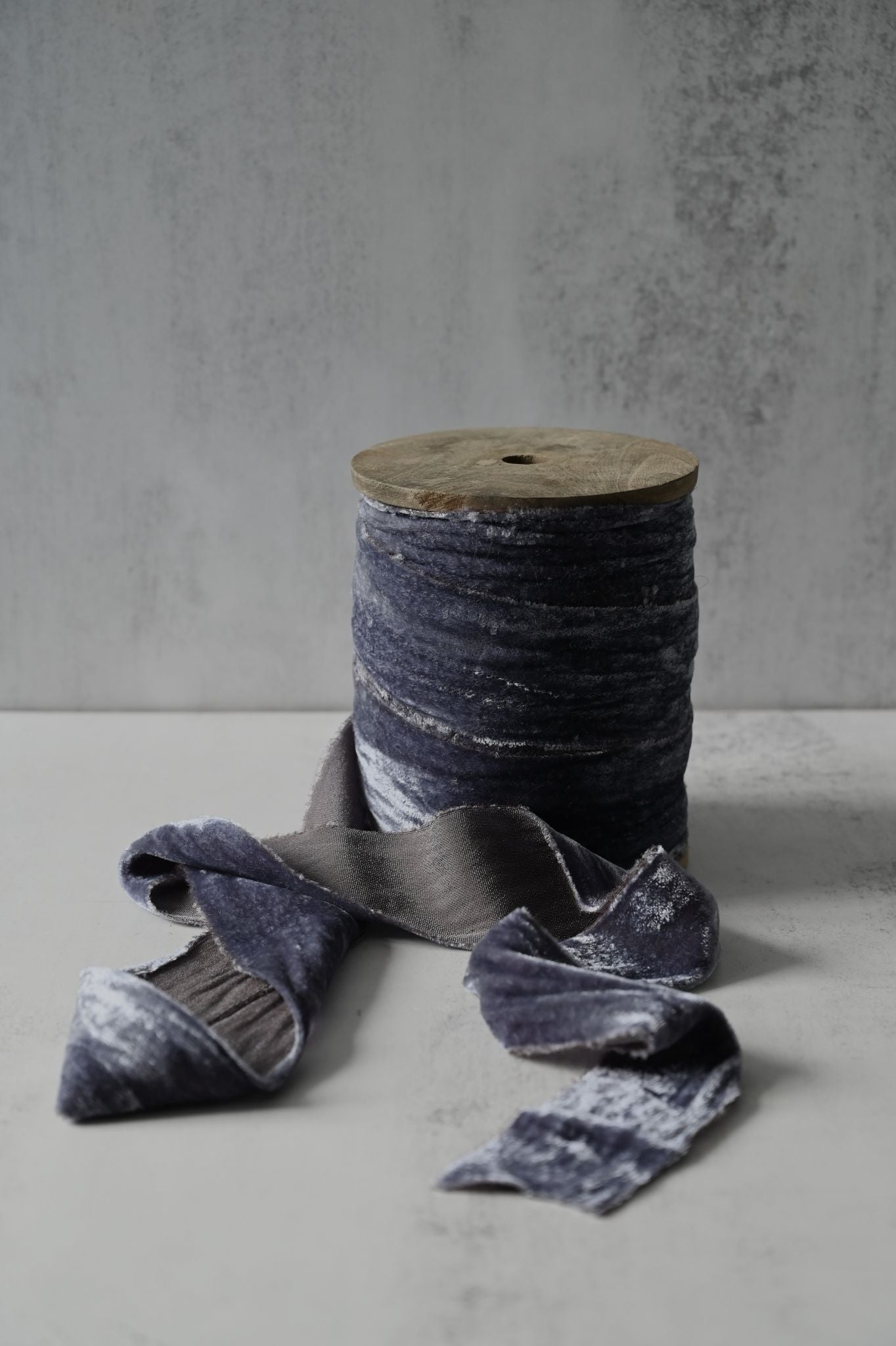 Wide graphite grey crushed velvet ribbon with frayed edges on a wooden spool.