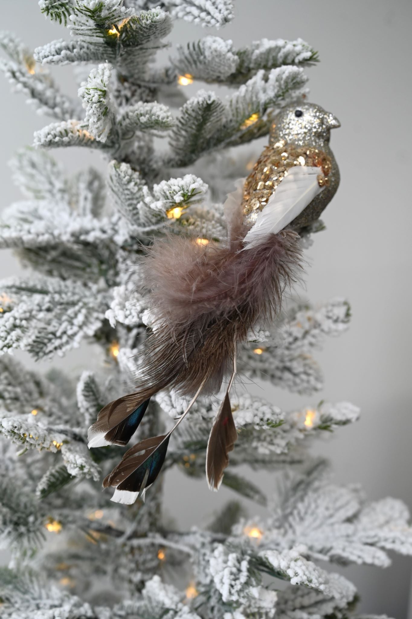 Silver glitter clip-on bird ornament with feather tail on a flocked Christmas tree.