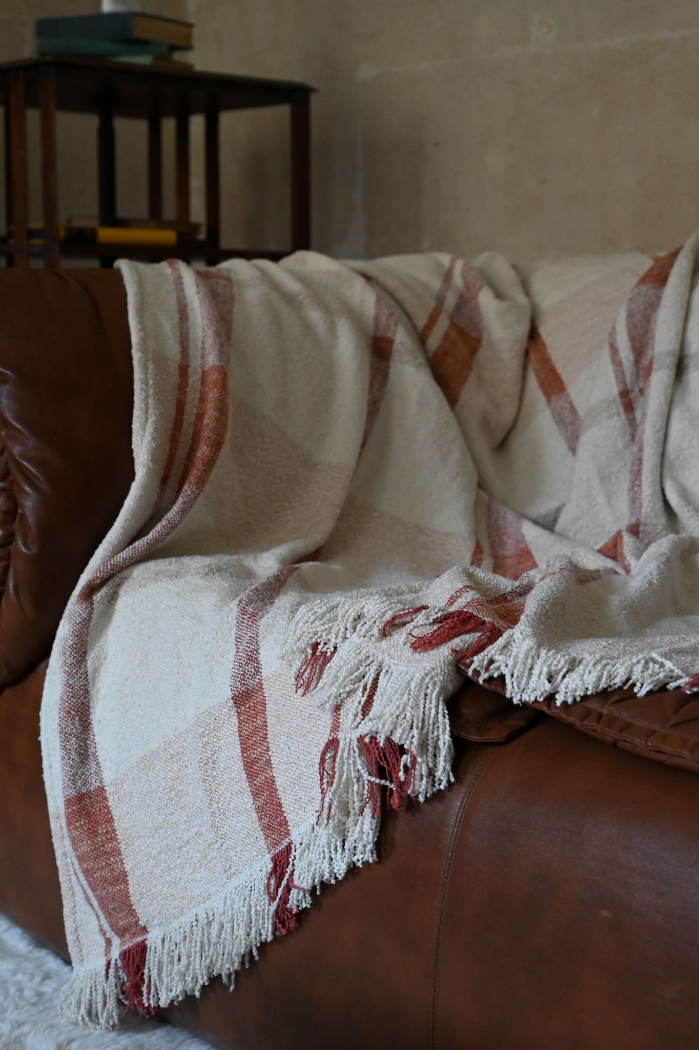 Woven rust and cream chunky check throw blanket draped over a leather sofa.