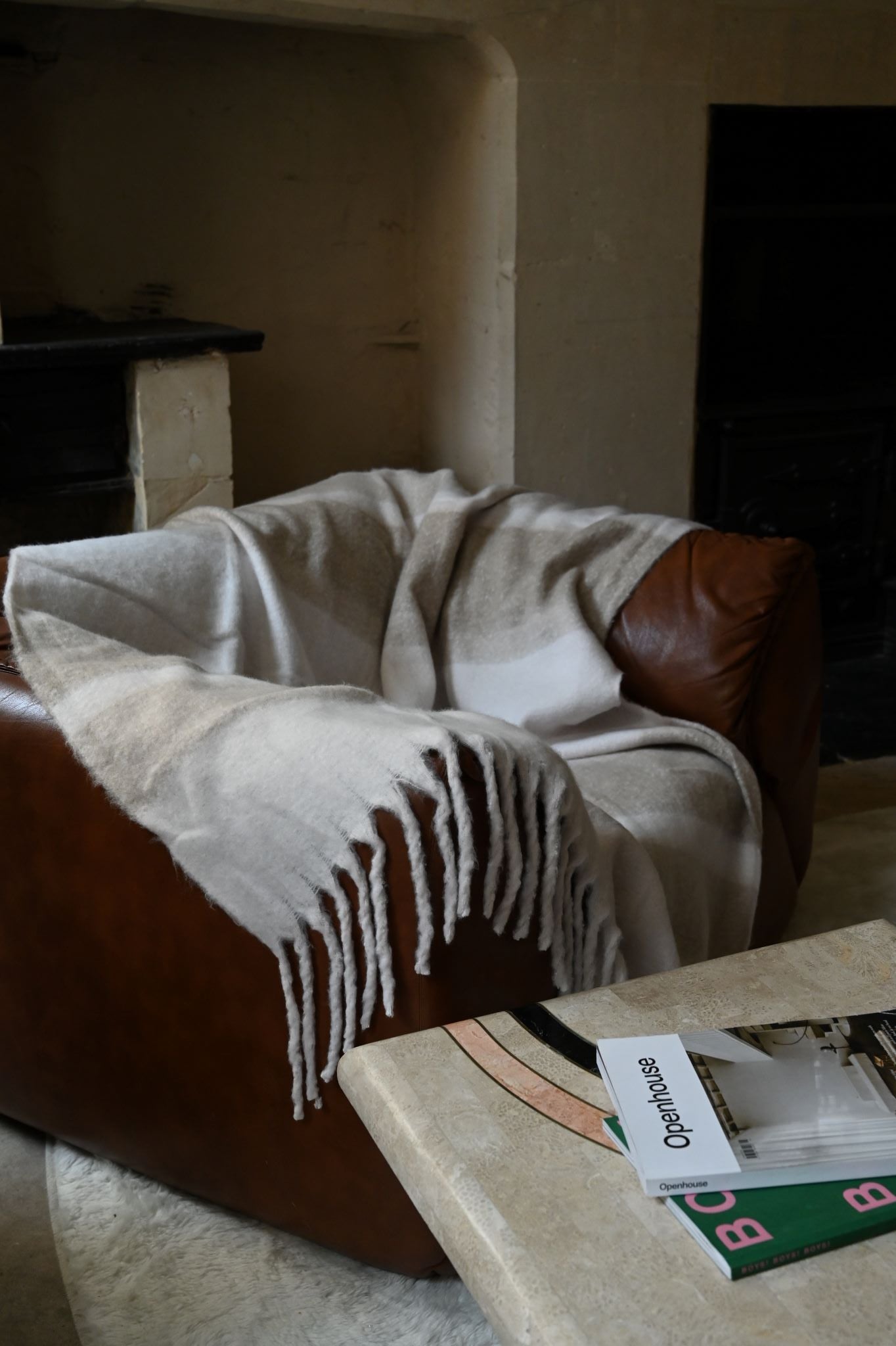 Neutral beige striped recycled throw blanket with chunky fringe draped over a leather armchair.