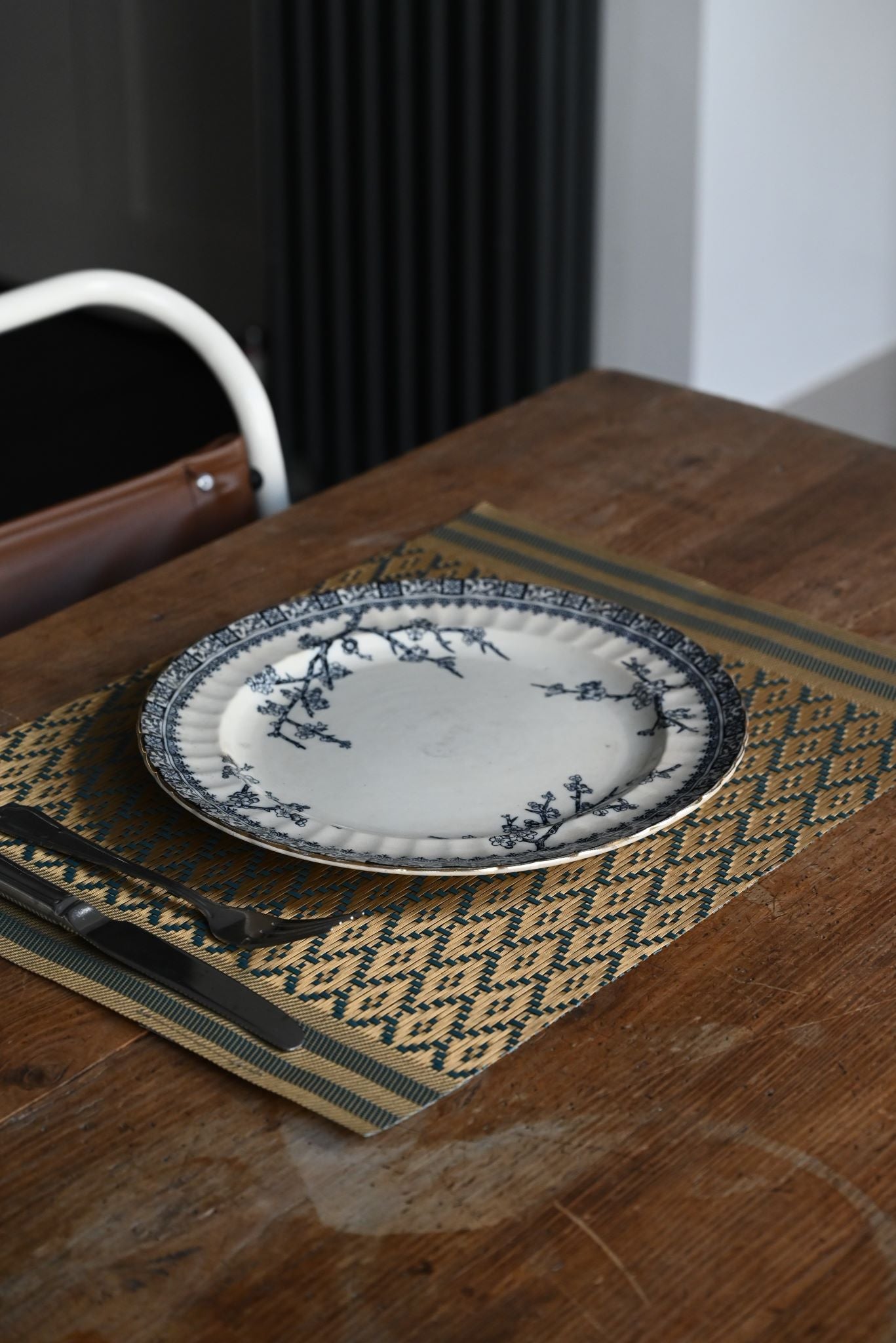 Black and gold woven diamond placemat under a ceramic plate on a wooden table.