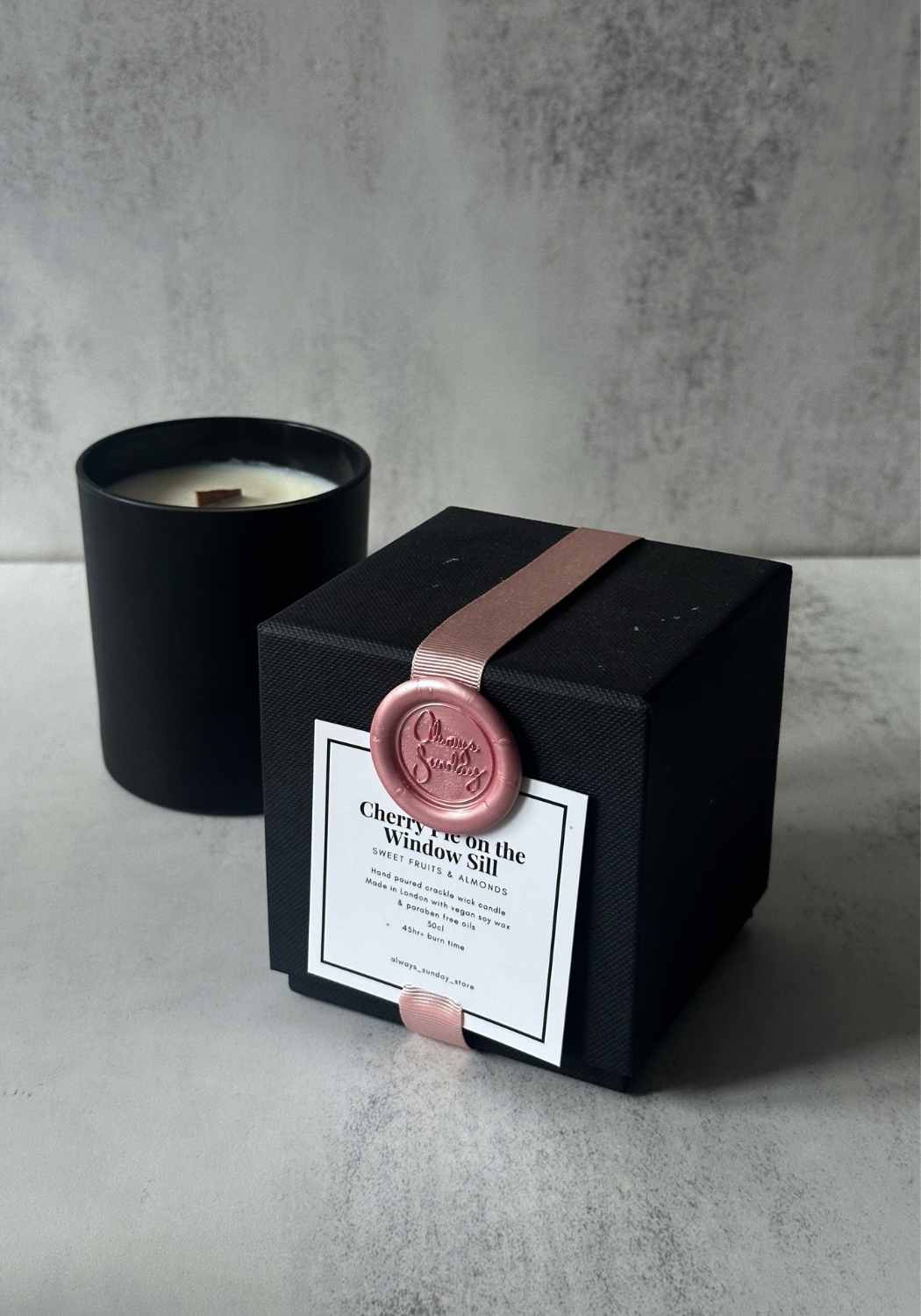Matte black scented candle with wooden wick and matching luxury gift box with ribbon seal.