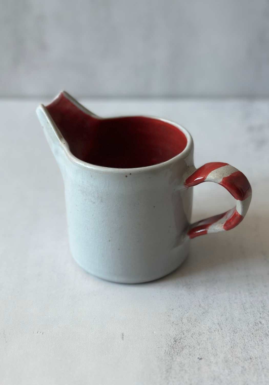 Handmade Welsh ceramic pouring jug with light blue glaze and red candy striped handle.