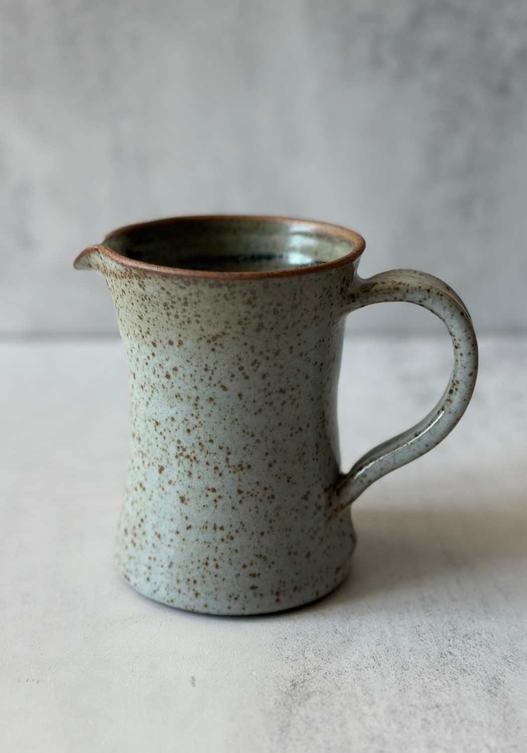 Handmade Welsh ceramic milk jug with speckled grayish-blue glaze and rustic brown rim.