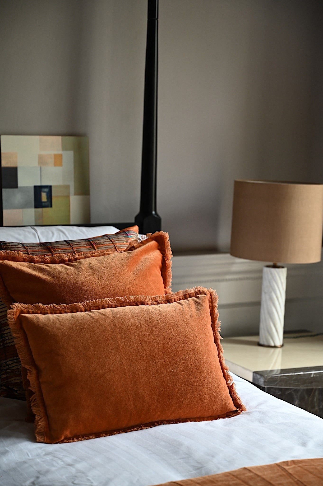 Rust orange fringed velvet lumbar cushions styled on a white luxury bed.
