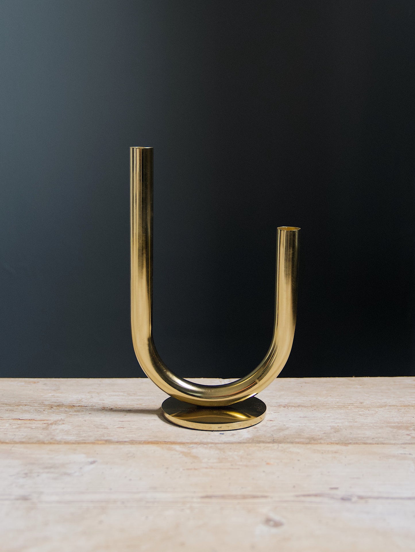 a large curvy gold candle holder with a round base on a dark background
