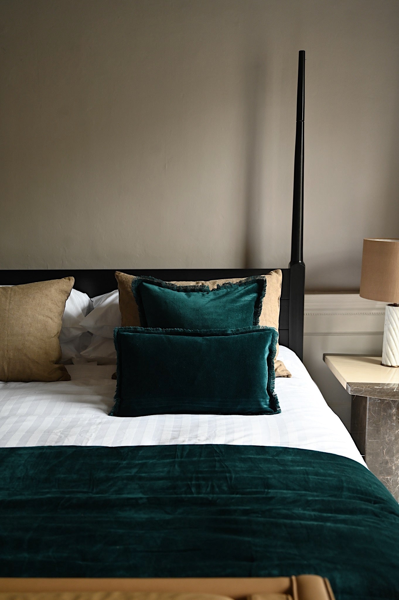 Deep emerald green fringed velvet cushions and throw on a luxurious bed setting.