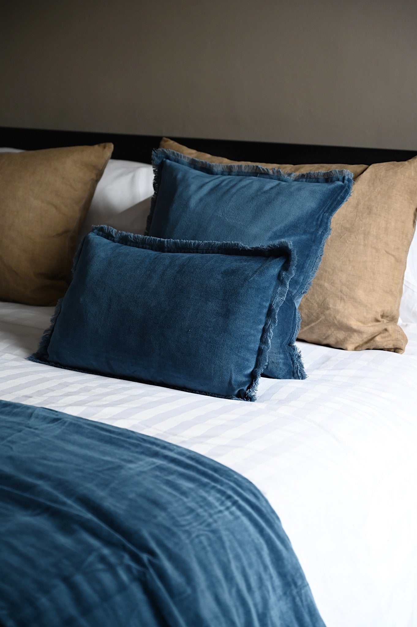 Layered cobalt blue fringed velvet cushions and throw styled on a bed.