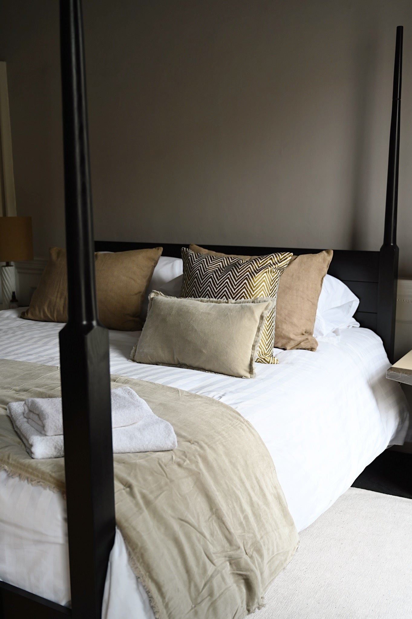 Luxurious taupe fringed velvet cushions and throw layered on a neutral bed.