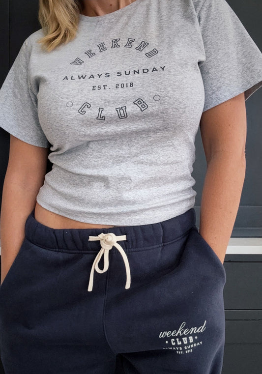 Person wearing a gray 'Weekend Club' t-shirt and navy pants with white text.