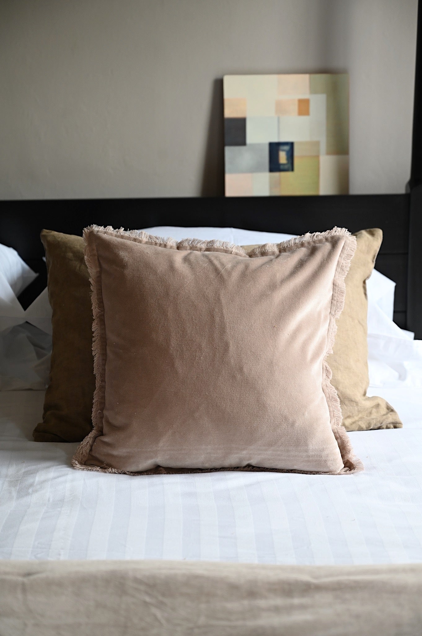 Nude beige fringed velvet cushions and throw layered on a white bed with modern decor.