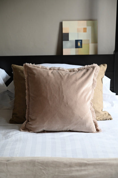 Nude beige fringed velvet cushions and throw layered on a white bed with modern decor.