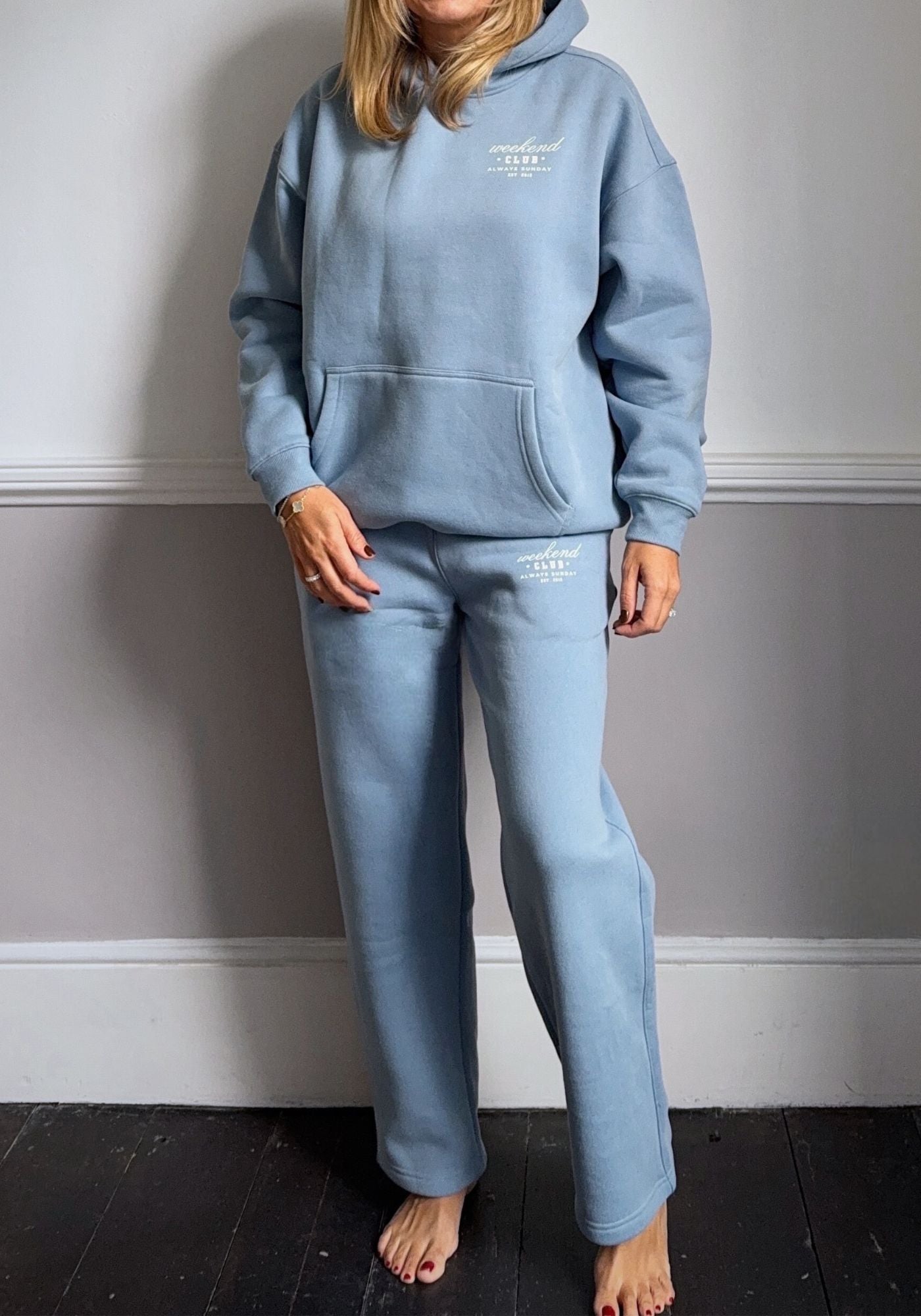 Person wearing a light blue hoodie and pants set against a gray wall.