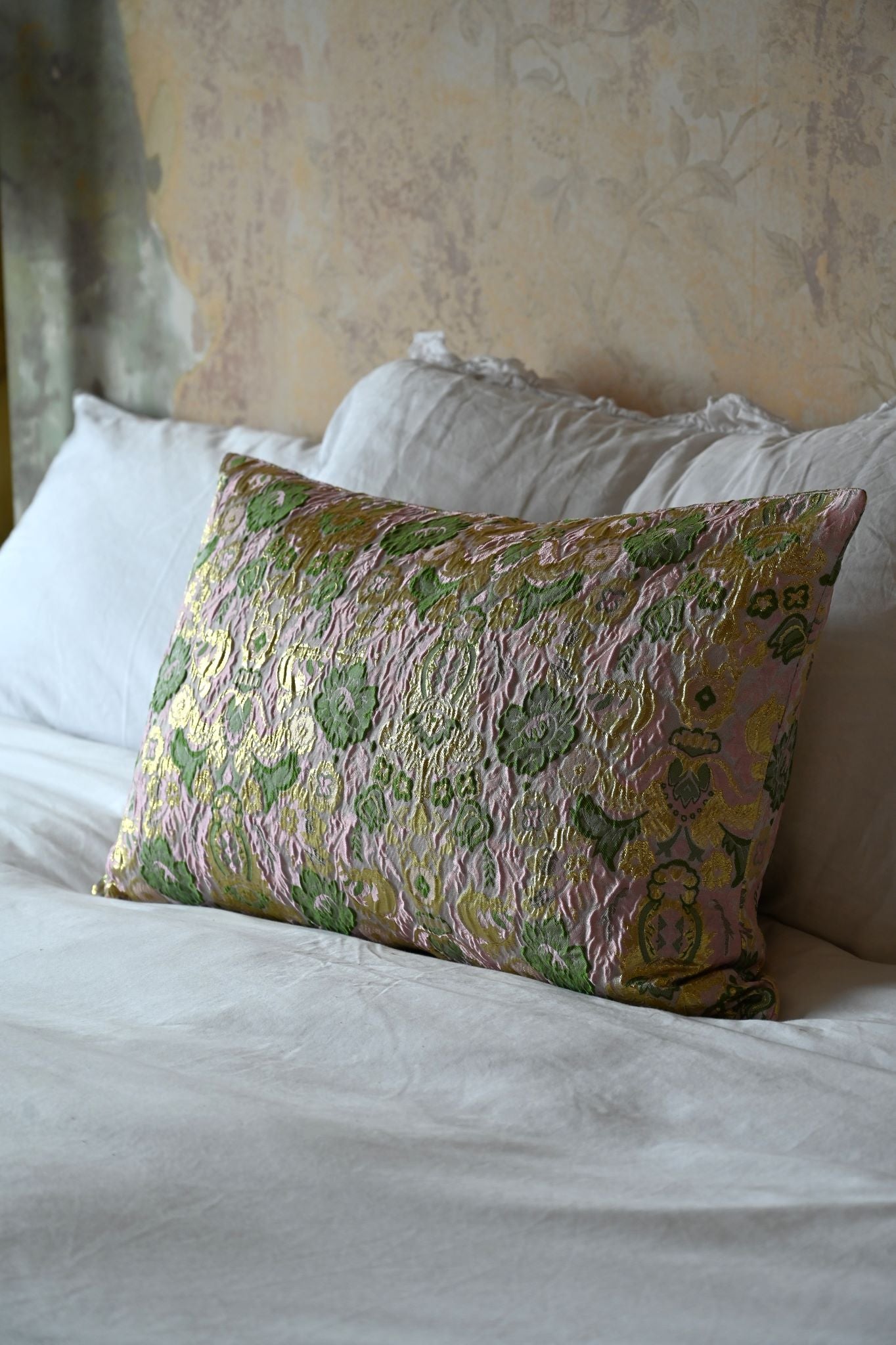 Rectangular pink and gold floral brocade cushion with metallic thread on white bedding.
