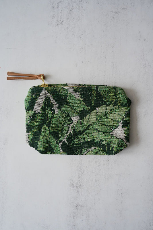 Two green tropical leaf-patterned tapestry pouches with gold zippers on a wooden table.