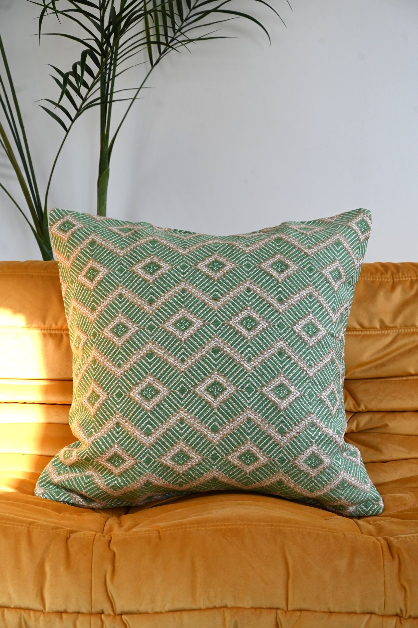 Square green and beige woven cushion with geometric diamond pattern on a yellow sofa.