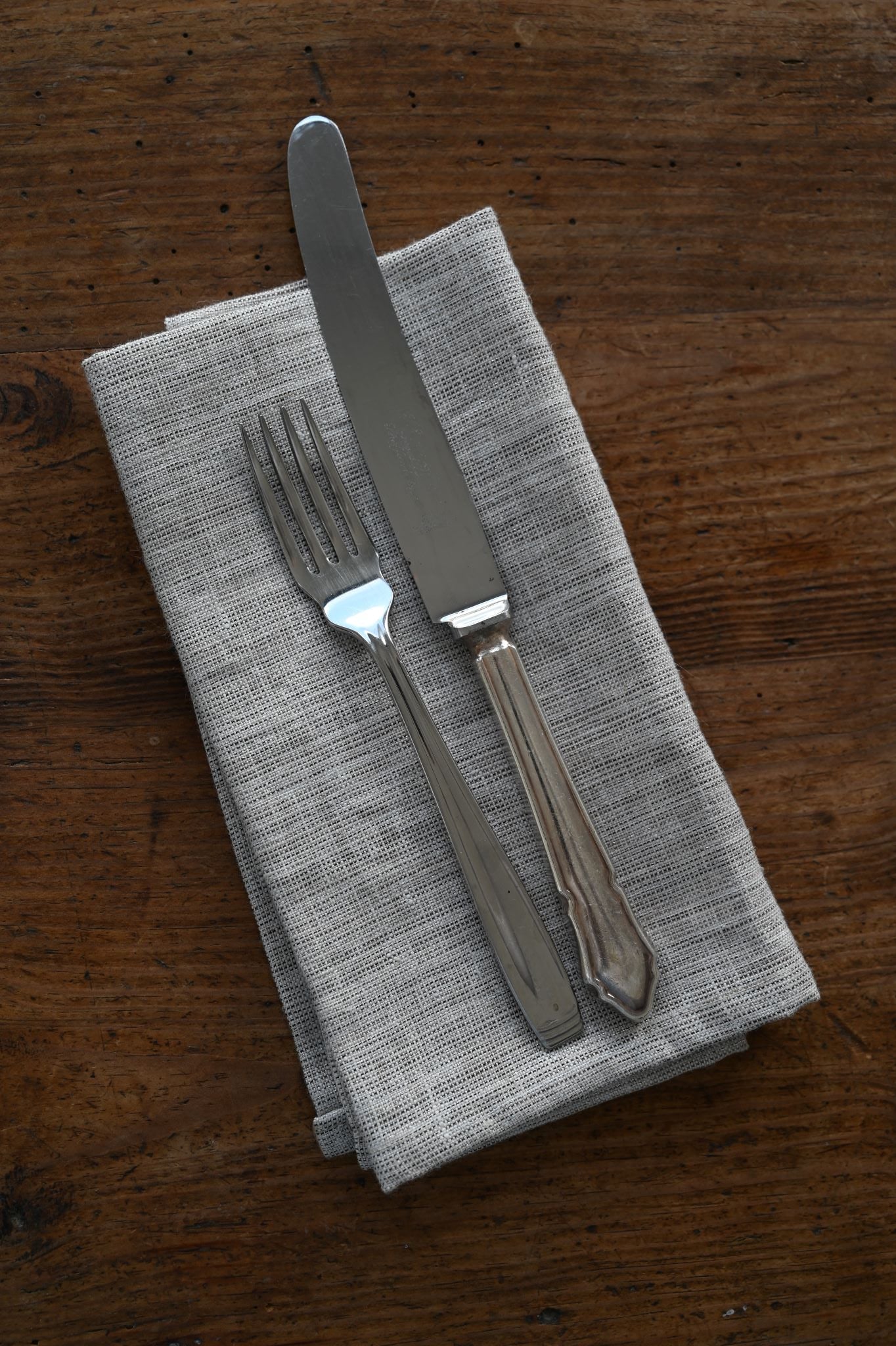 Heather grey metallic table napkin with silver cutlery on a rustic wooden surface.