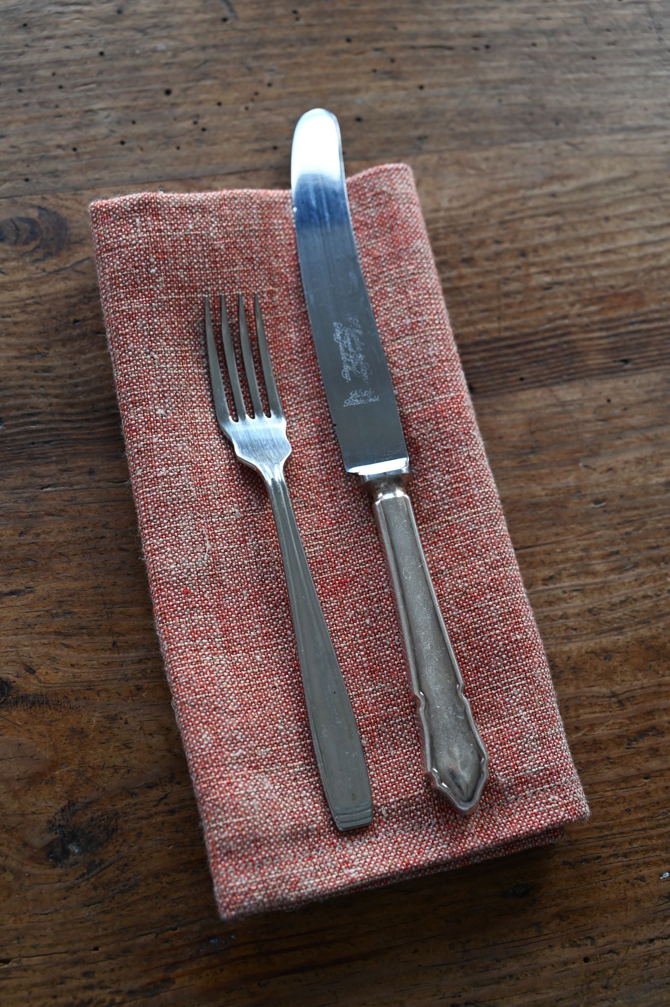 Textured pink-hued red metallic napkin set with vintage silver cutlery on a dark wood table.