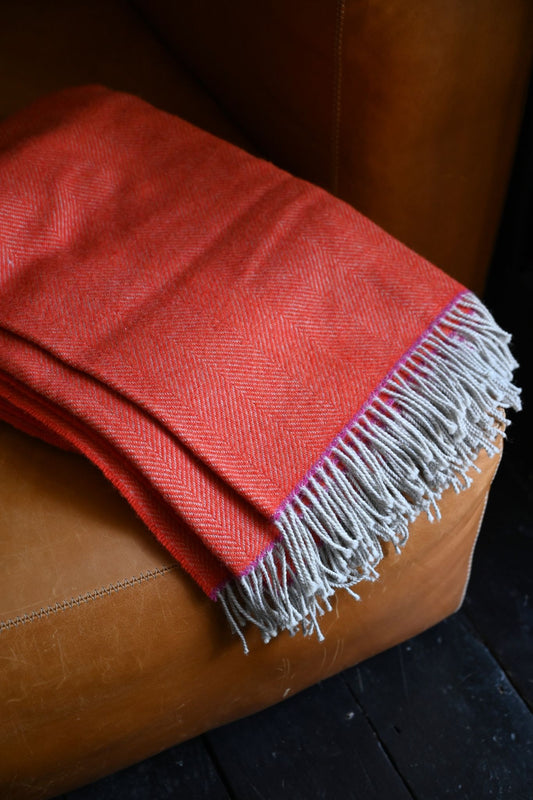 Red blanket with white fringe draped over a brown leather chair.